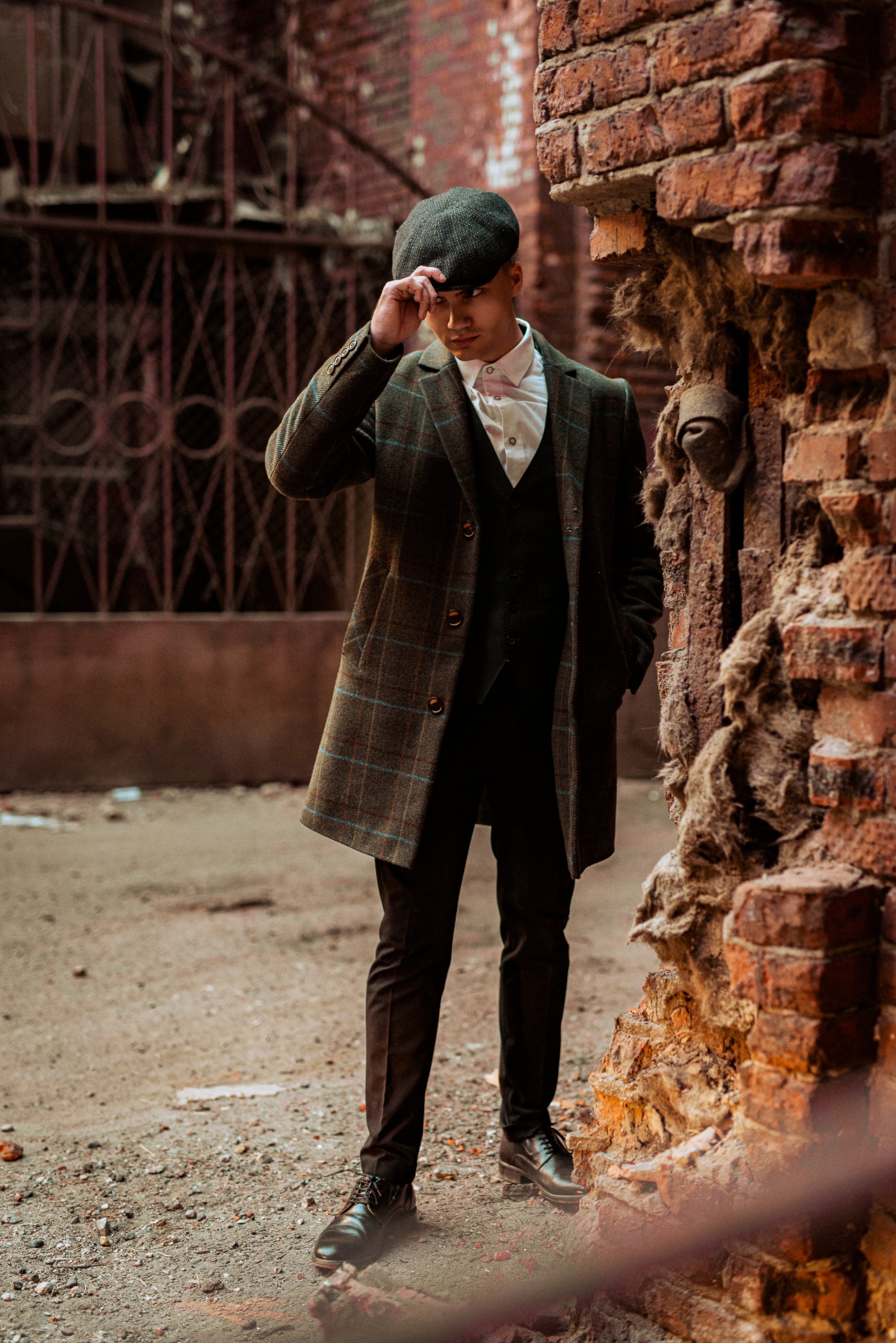 Фотосессия в стиле «Острых козырьков» для молодого парня в полный рост на фоне завода из красного кирпича