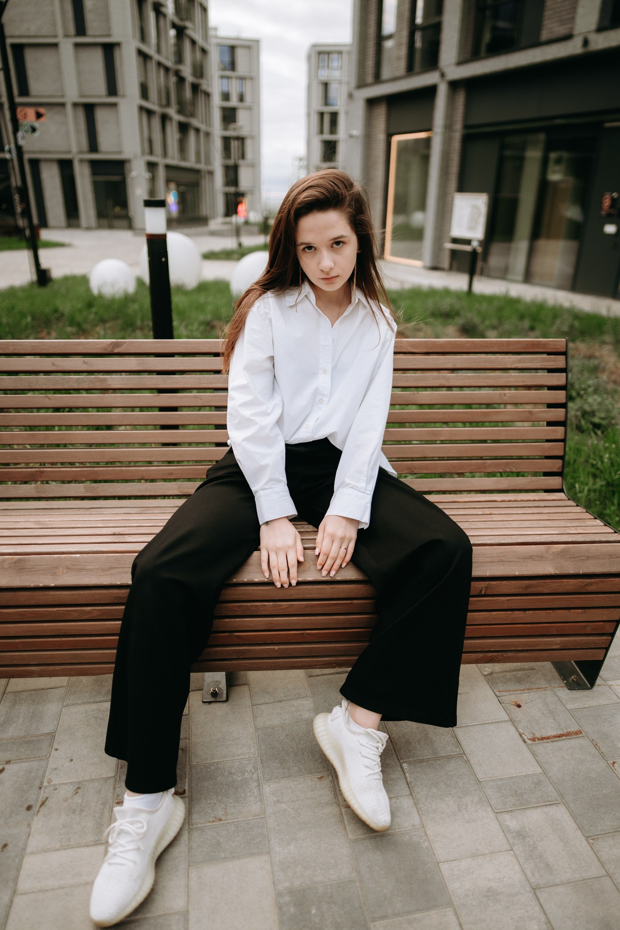 Уличный fashion-портрет: образ с белой рубашкой, широкими черными брюками и светлыми кроссовками, геометрия городского квартала