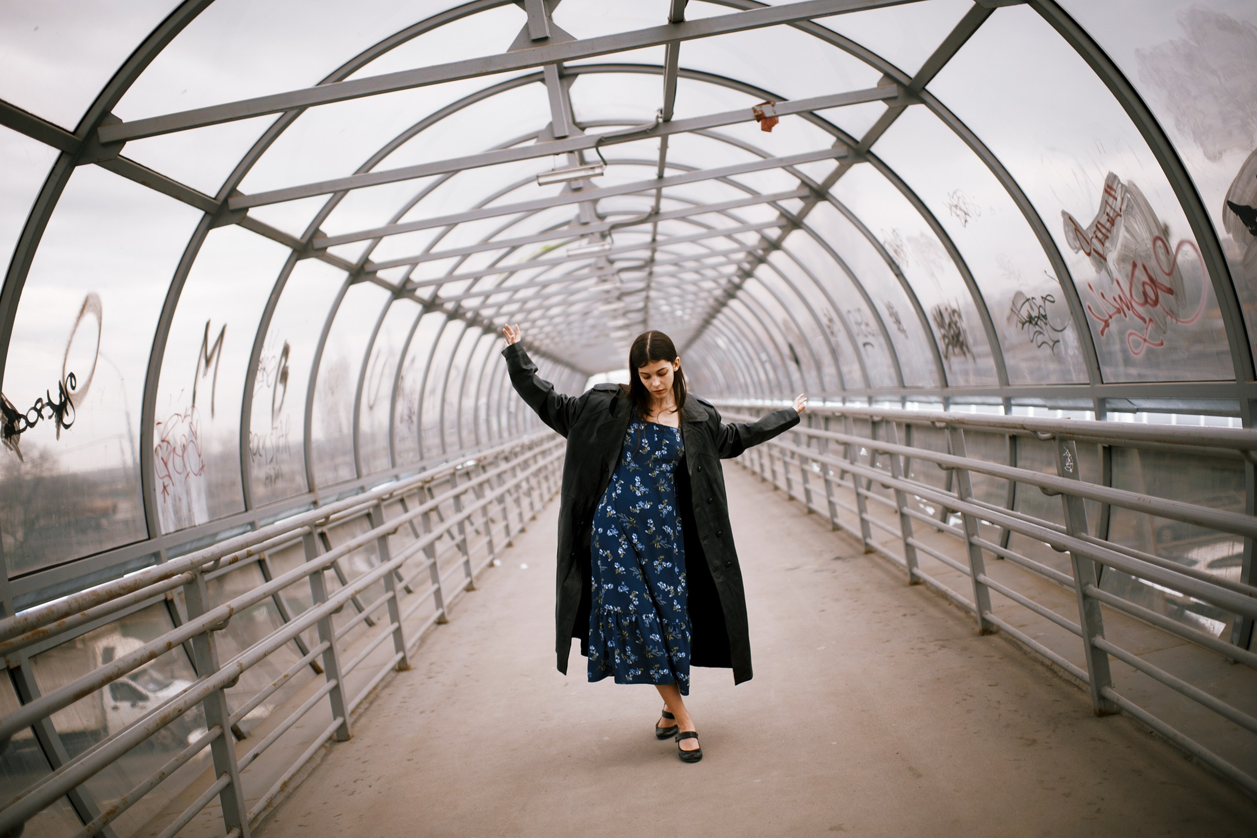 Девушка в черном плаще гуляет по надземному переходу