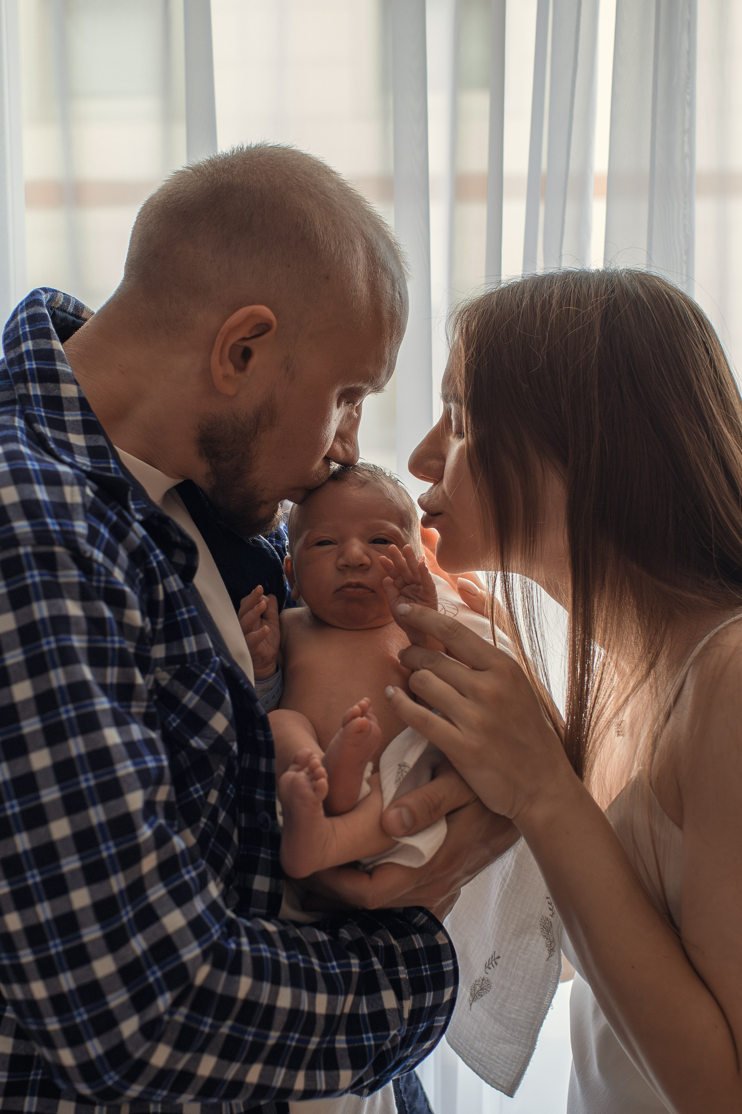 Общий план палаты: счастливые родители стоят у окна с ребёнком на руках.