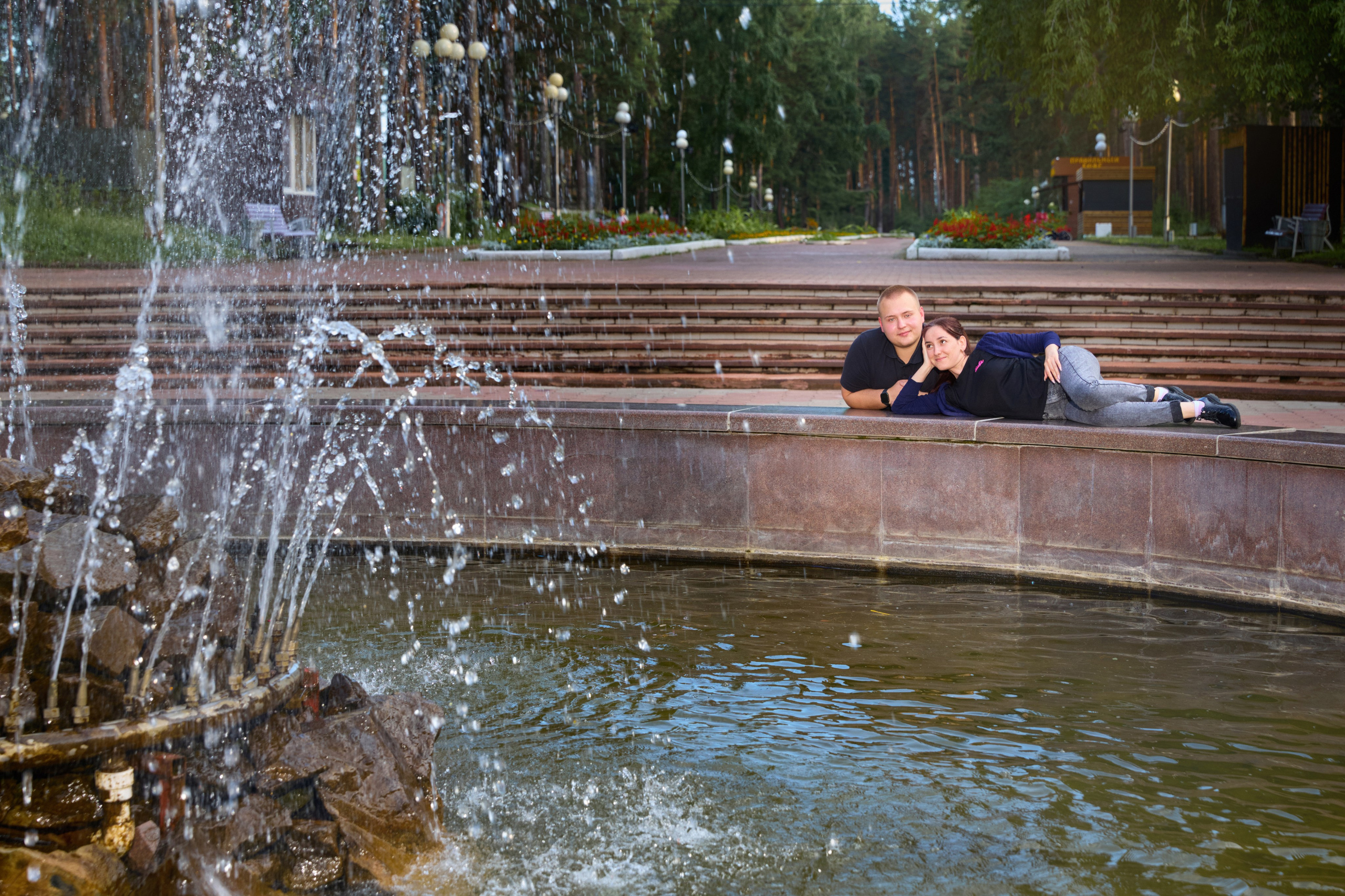 девушка лежит,  согнув колено на ограждении фонтана, парень облокотился на ограждение