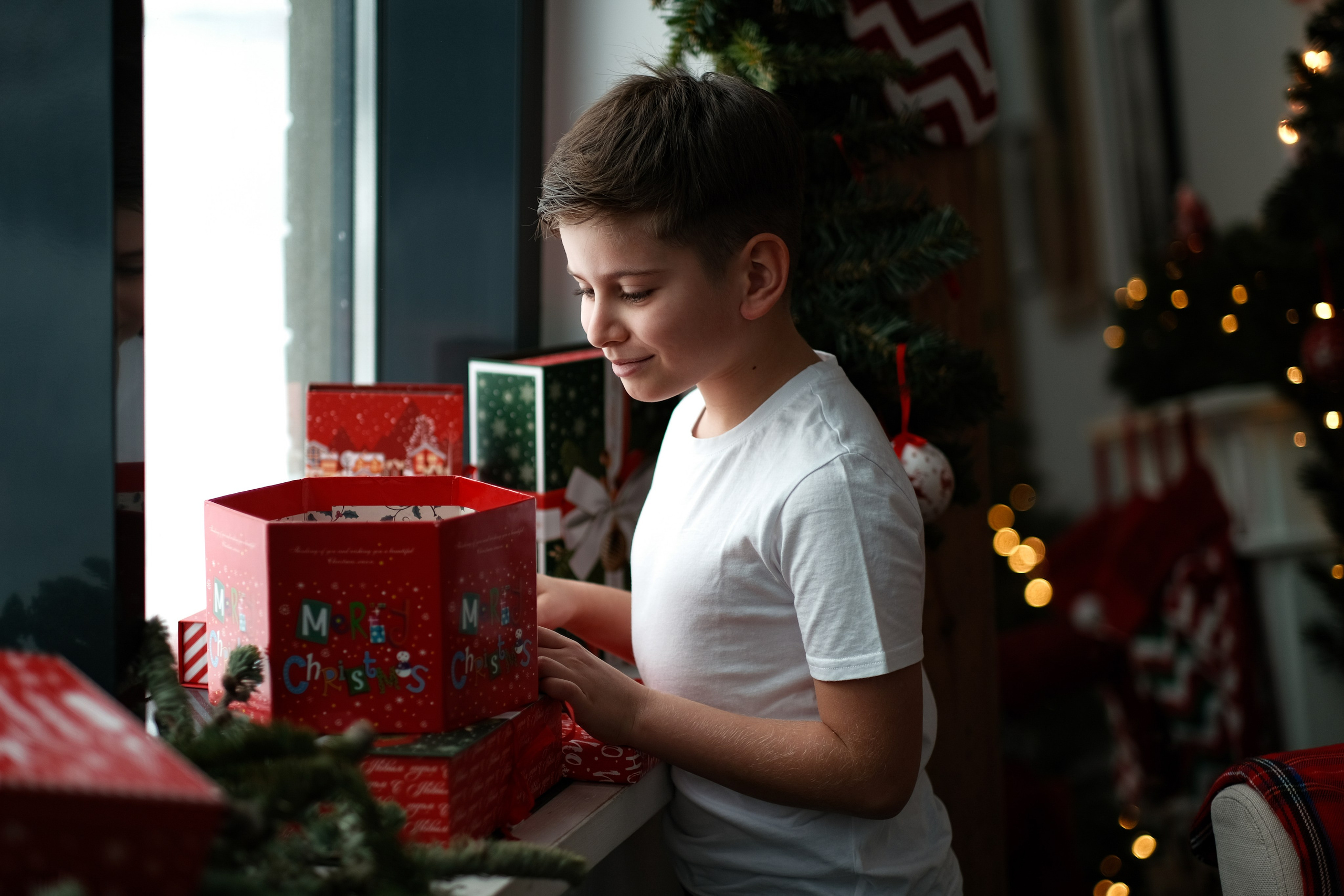 Мальчик смотрит на подарки к новому году. Фото у окна.