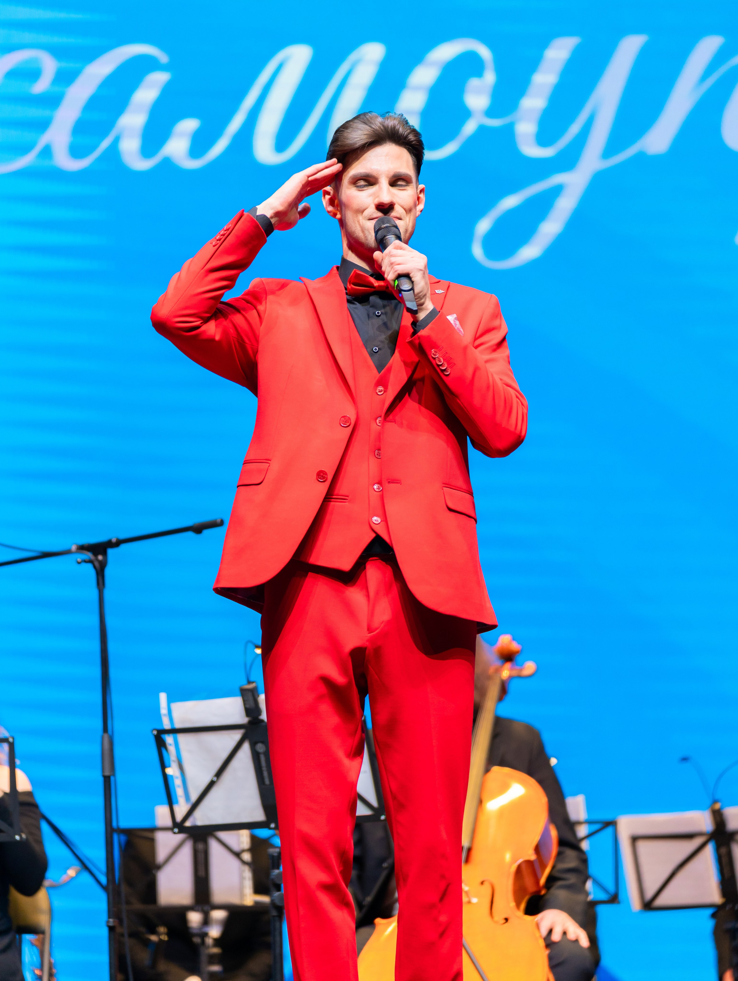 Солист в красном костюме с микрофоном исполняет песню и отдаёт честь зрителям на празднике Дня местного самоуправления в Санкт-Петербурге | Фото: Евгений Мальцев.
