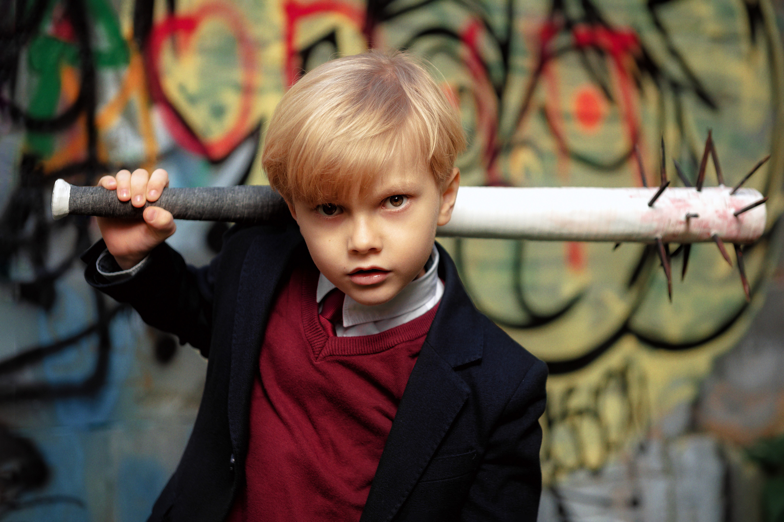 Мальчик в школьной форме с бейсбольной битой с шипами на плече смотрит в камеру