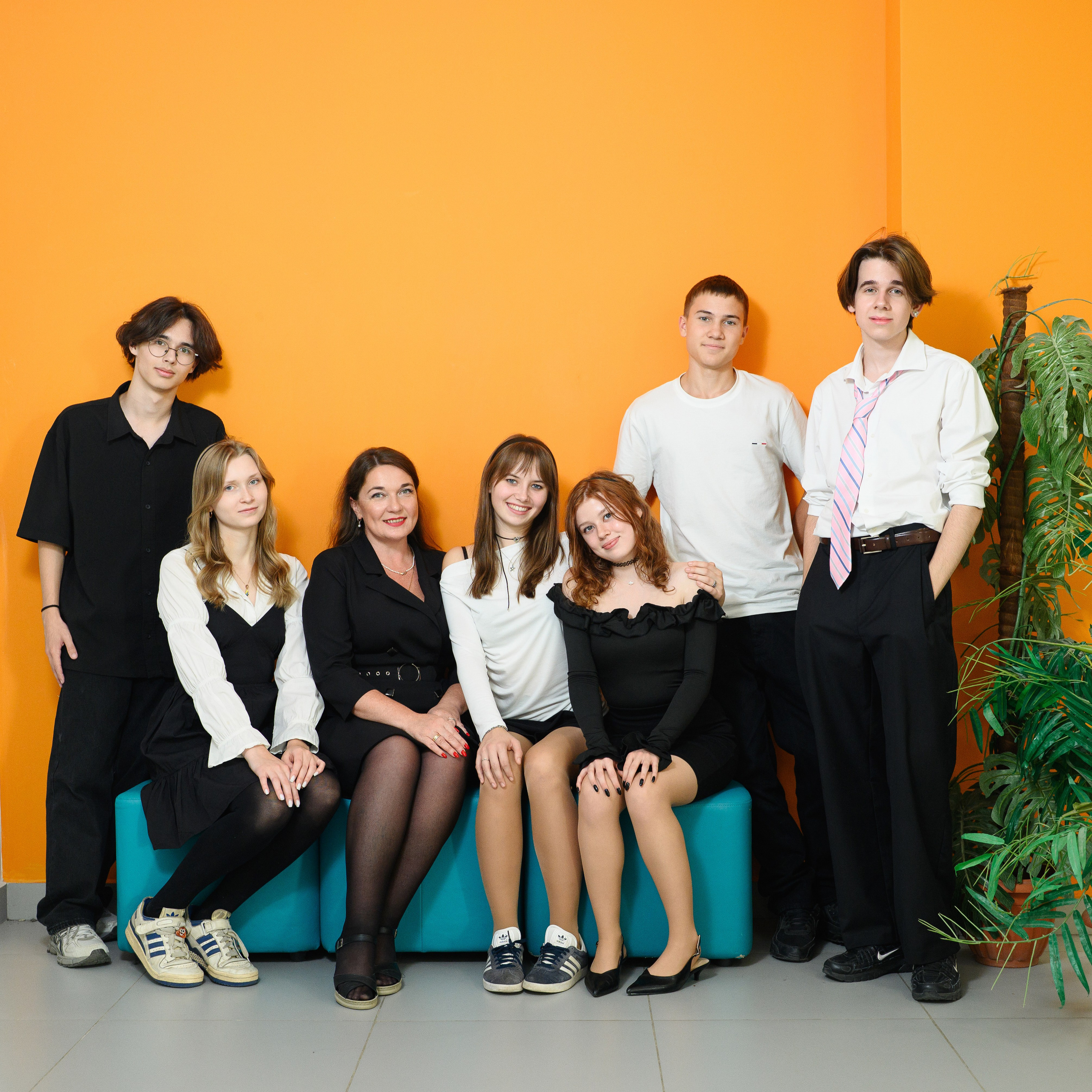 Ученики 9 класса и педагог позируют на диване у яркой оранжевой стены.