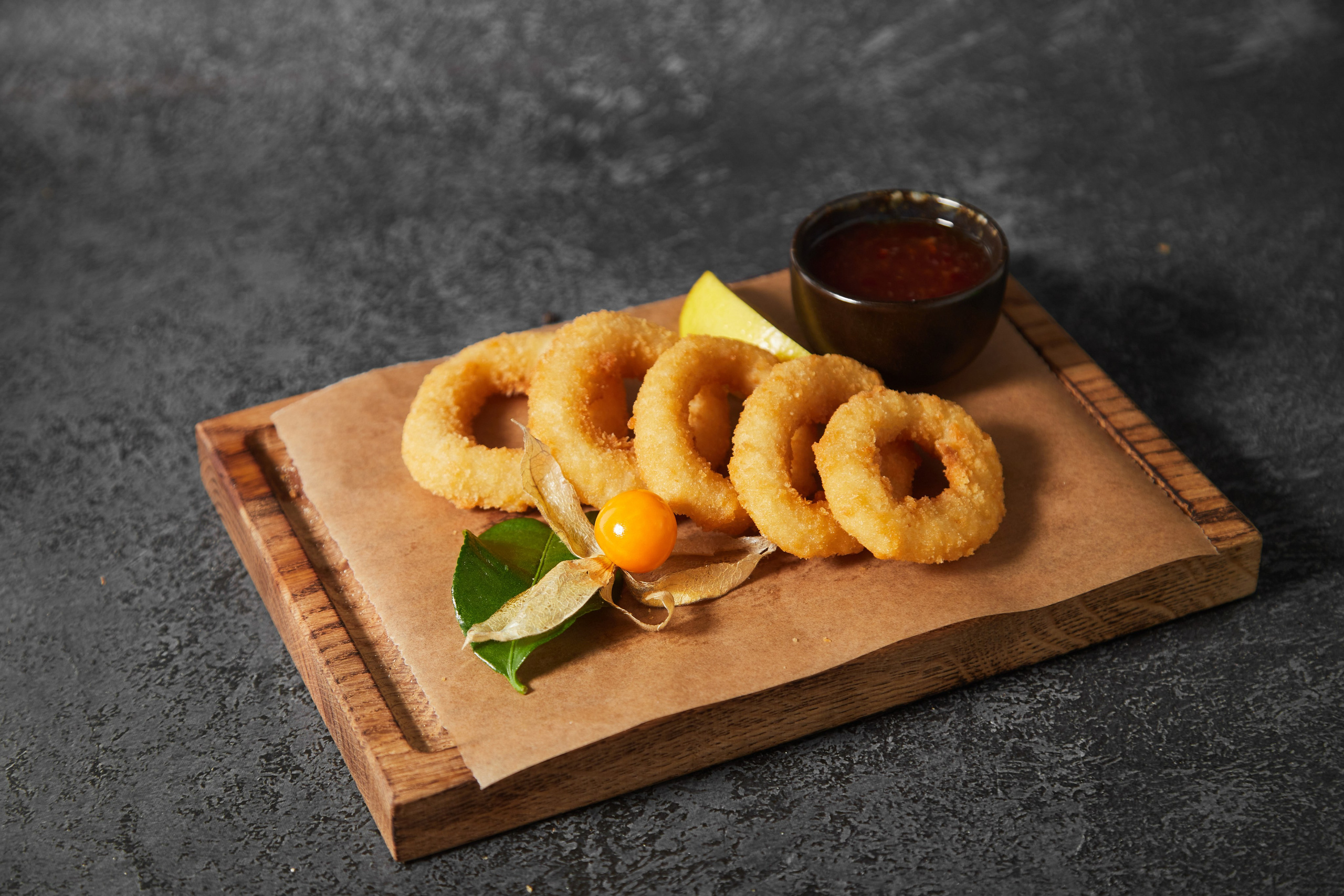 Луковые кольца с соусом на деревянной доске.