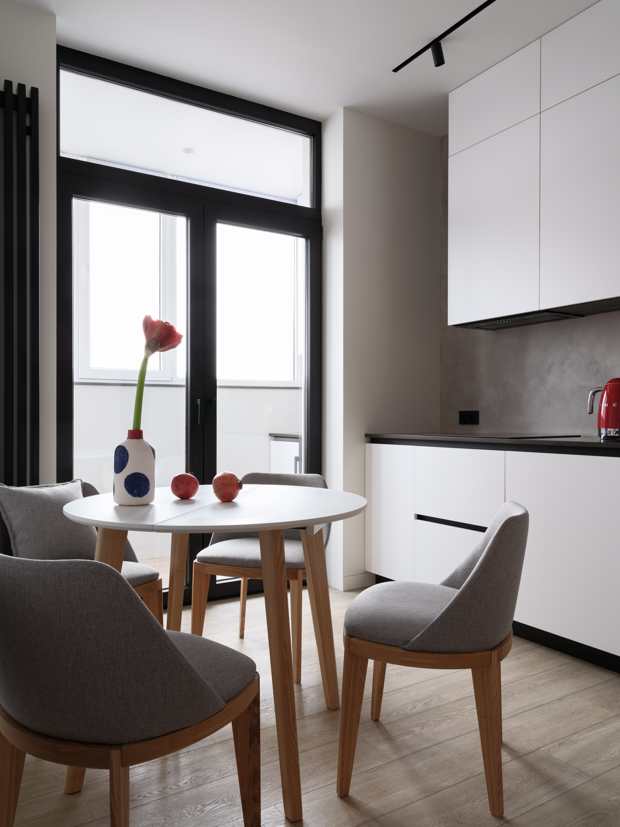Минималистичная кухня с белыми фасадами, деревянным полом и обеденной зоной с круглым столом и серыми стульями. Дизайн интерьера от Евгении Княжевой и Владлены Приваловой, фото Сергея Денисенко