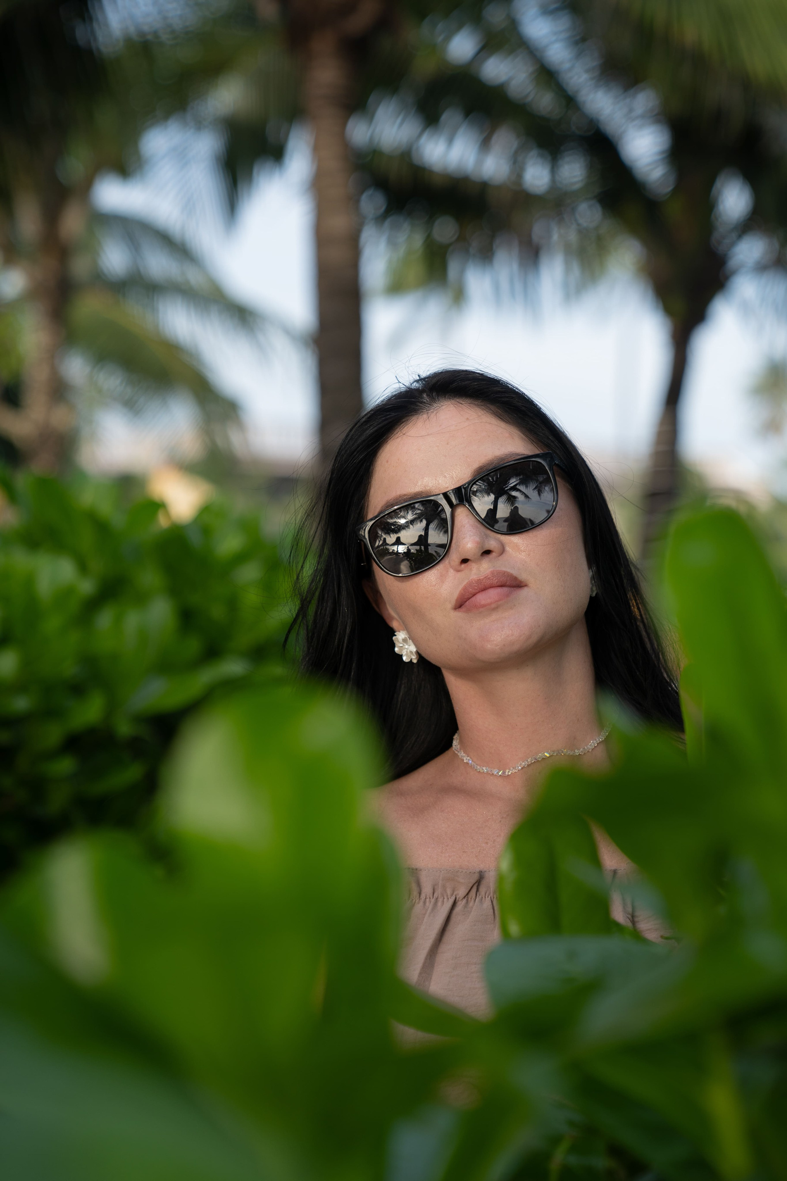 Загадочный женский образ: портрет девушки в очках, сделанный сквозь зеленые листья.