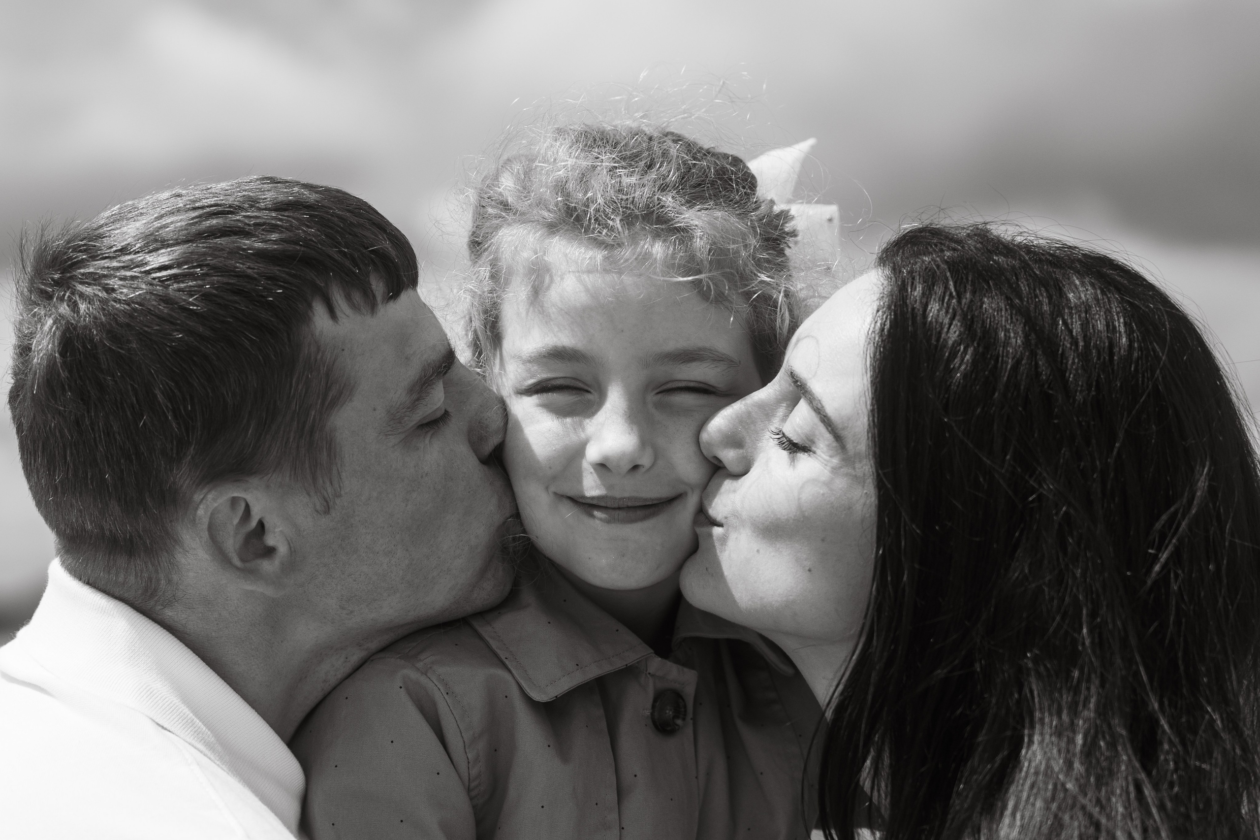 Родители целуют дочь в щёки, чёрно-белый кадр — семейная фотосессия у воды