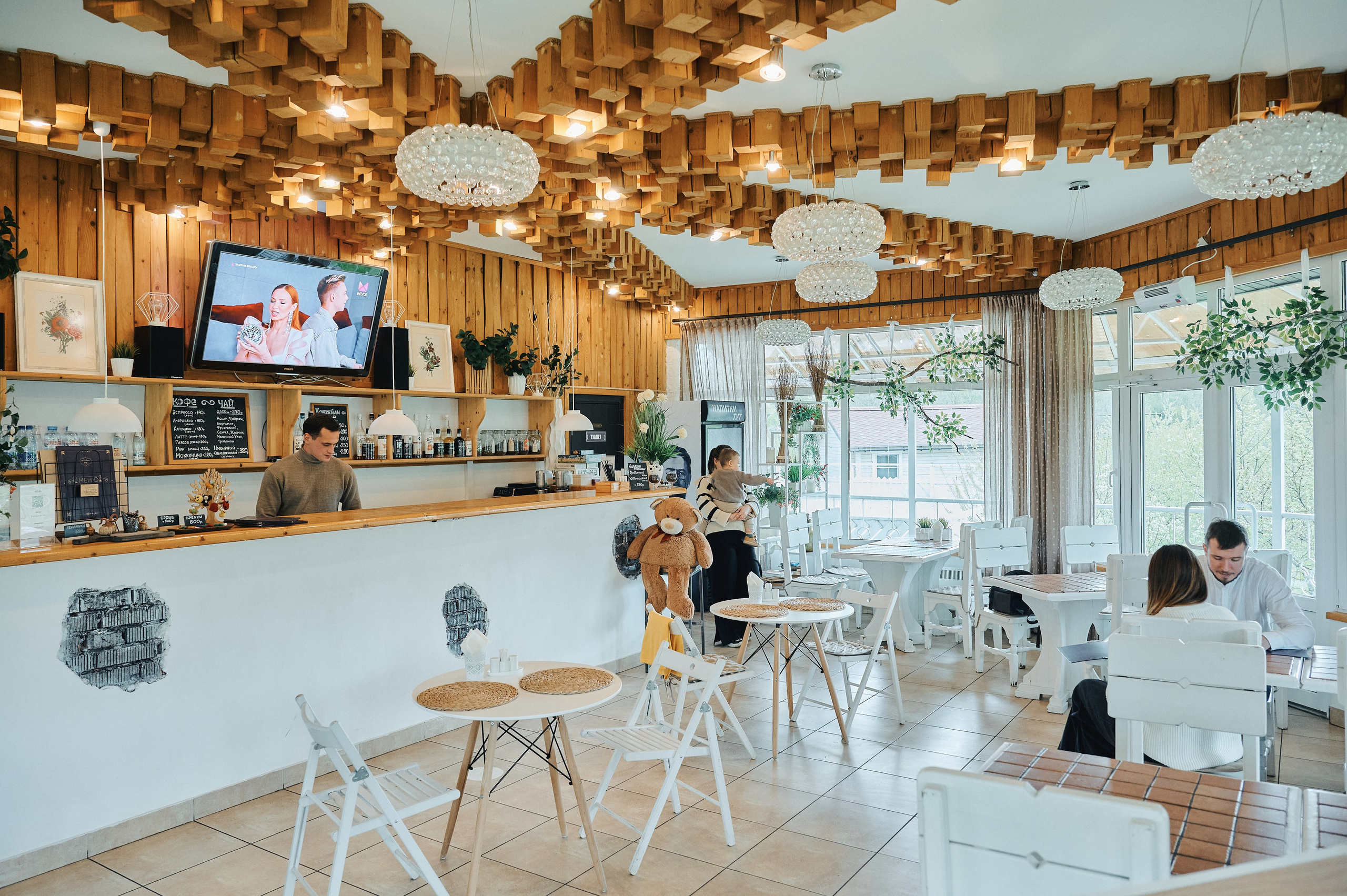 Обзорное фото интерьера кафе с белой мебелью, барной стойкой и деревянным потолком