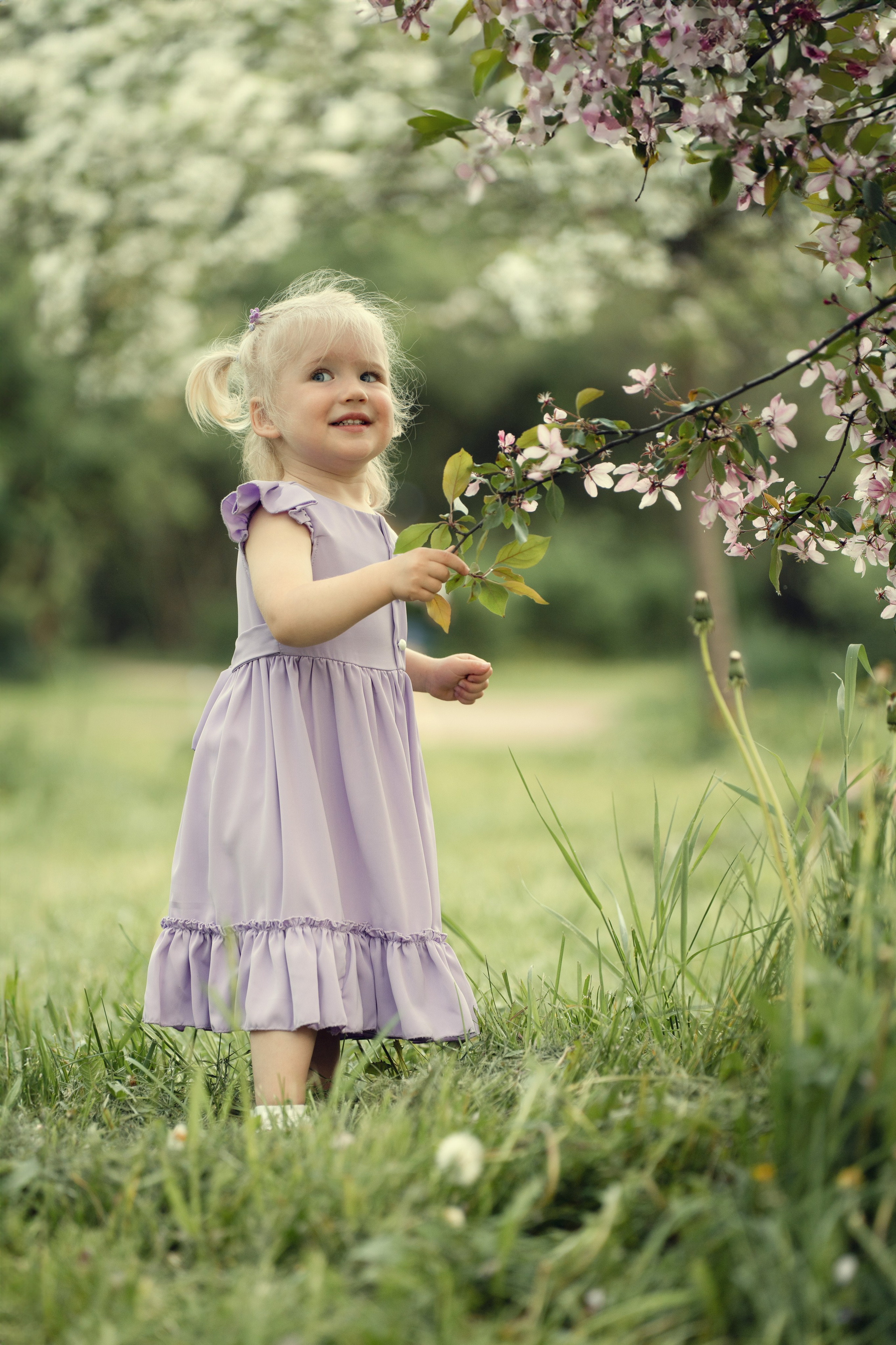 Маленькая девочка рассматривает цветочек в весеннем саду.