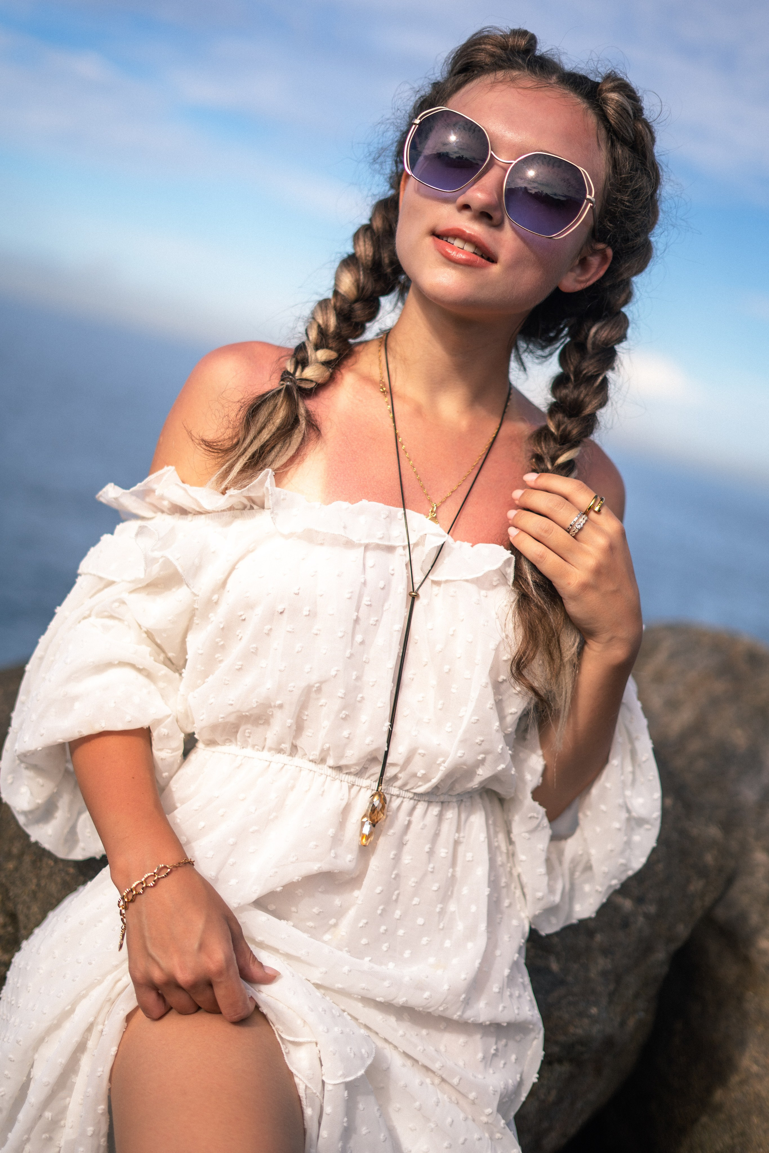 a girl in a white dress and glasses posing on the rocks at the water's edge