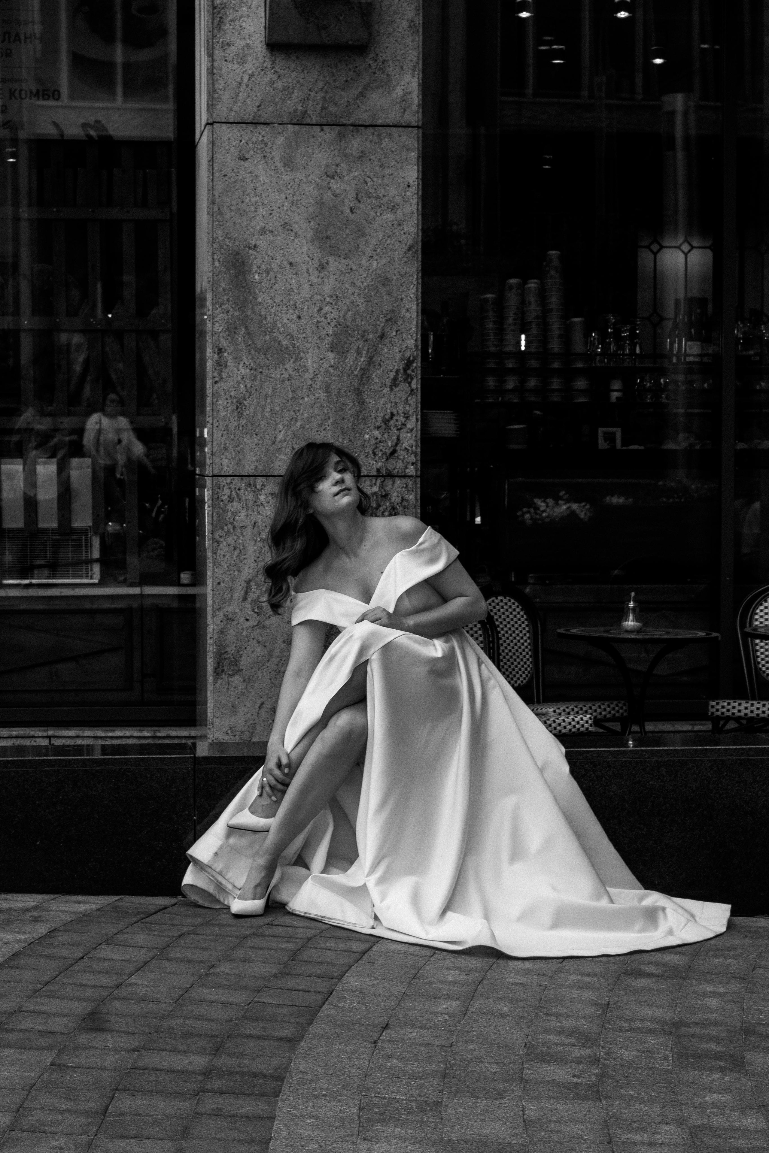 Невеста в длинном платье сидит на площади