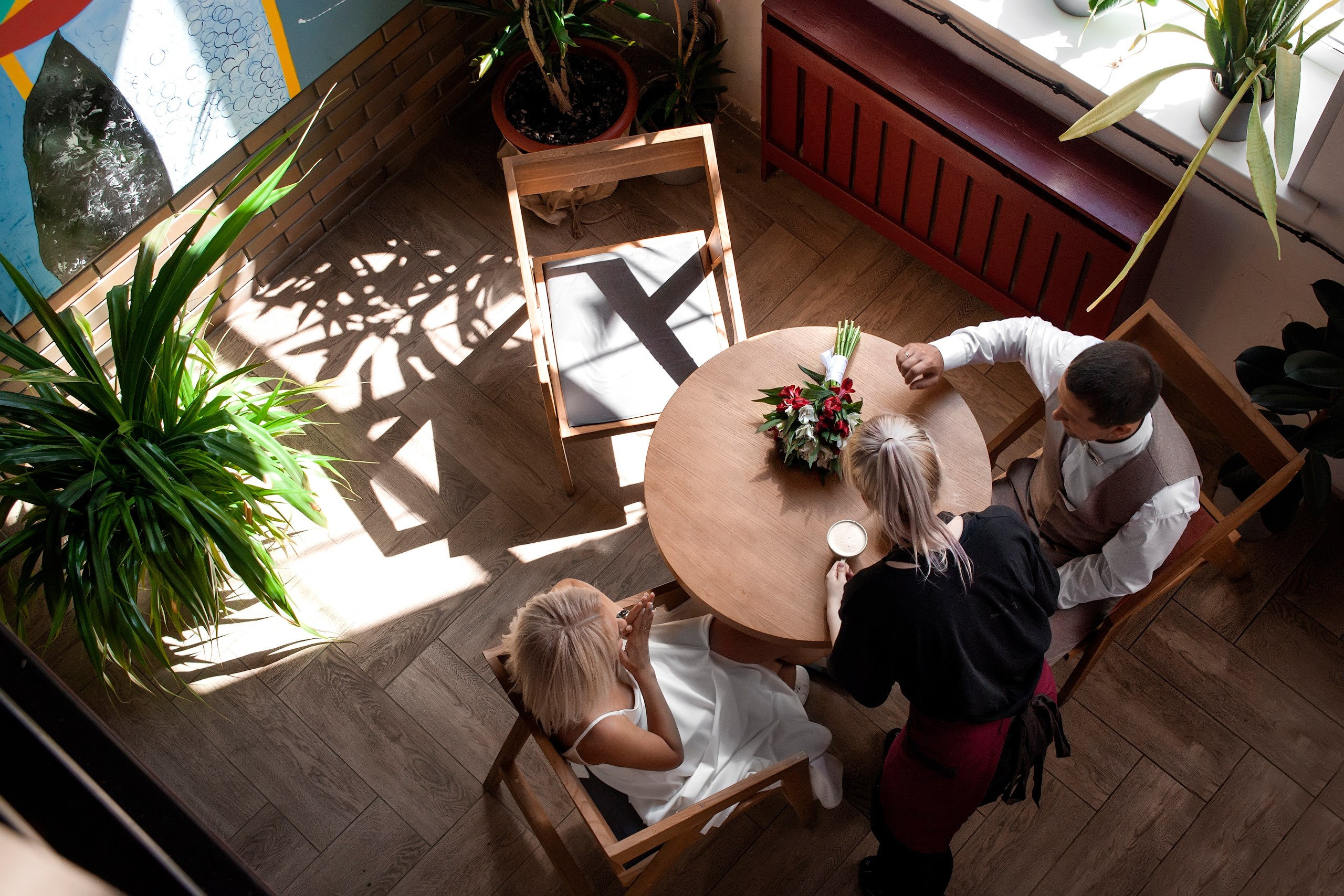 Официант кафе ставит на столик, за которым сидят жених и невеста, их заказ, на столике лежит свадебный букет - фотограф Янкаускене Наталья