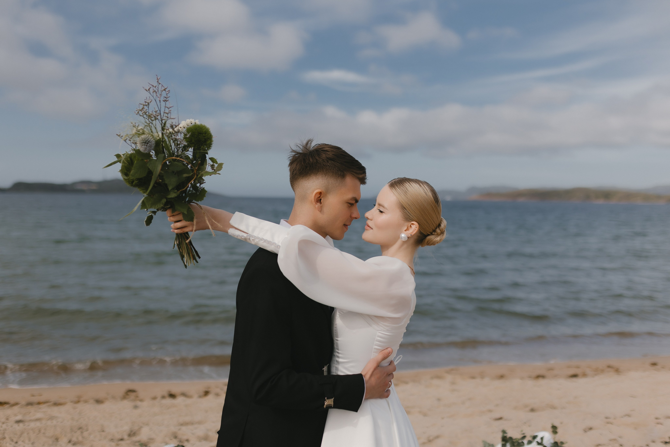 Парень нежно держит девушку за талию, запечатлеваясь на память на фоне морских волн.