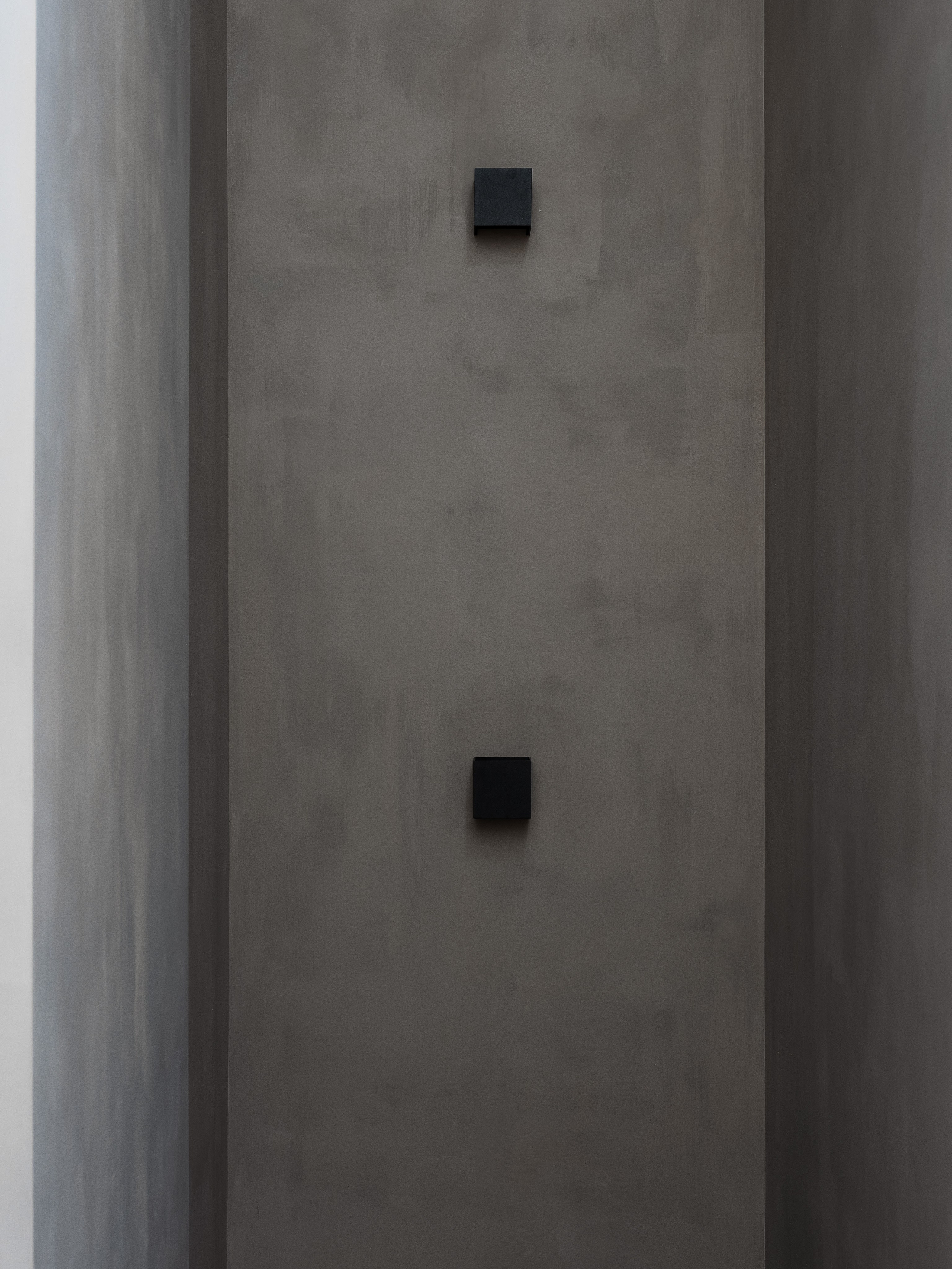 Узкий лестничный пролёт с чёрными квадратными бра на серой фактурной стене, подчёркивающий геометрию пространства. Интерьер в стиле минимализм от дизайнера Екатерины Мищенко, фотограф Сергей Денисенко, современный свет.