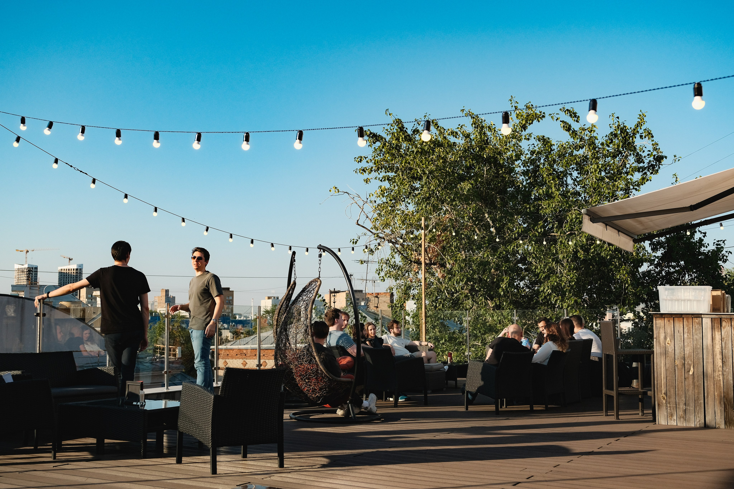 Вечеринка в Москве на крыше. Люди стоят на фоне синего неба. Гирлянды лампочек на фоне неба.