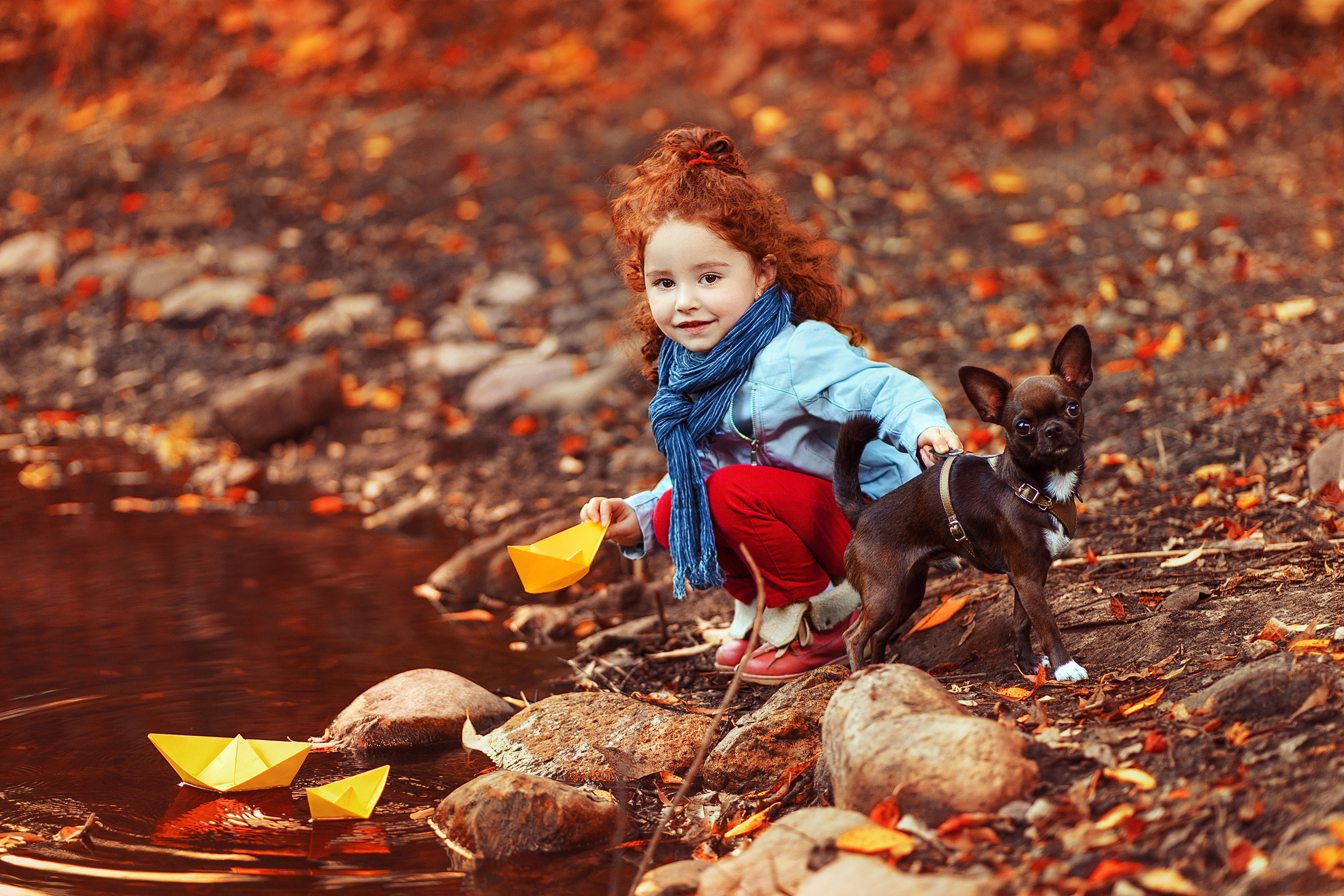 Девочка запускает кораблики в воду вместе со своей собакой.