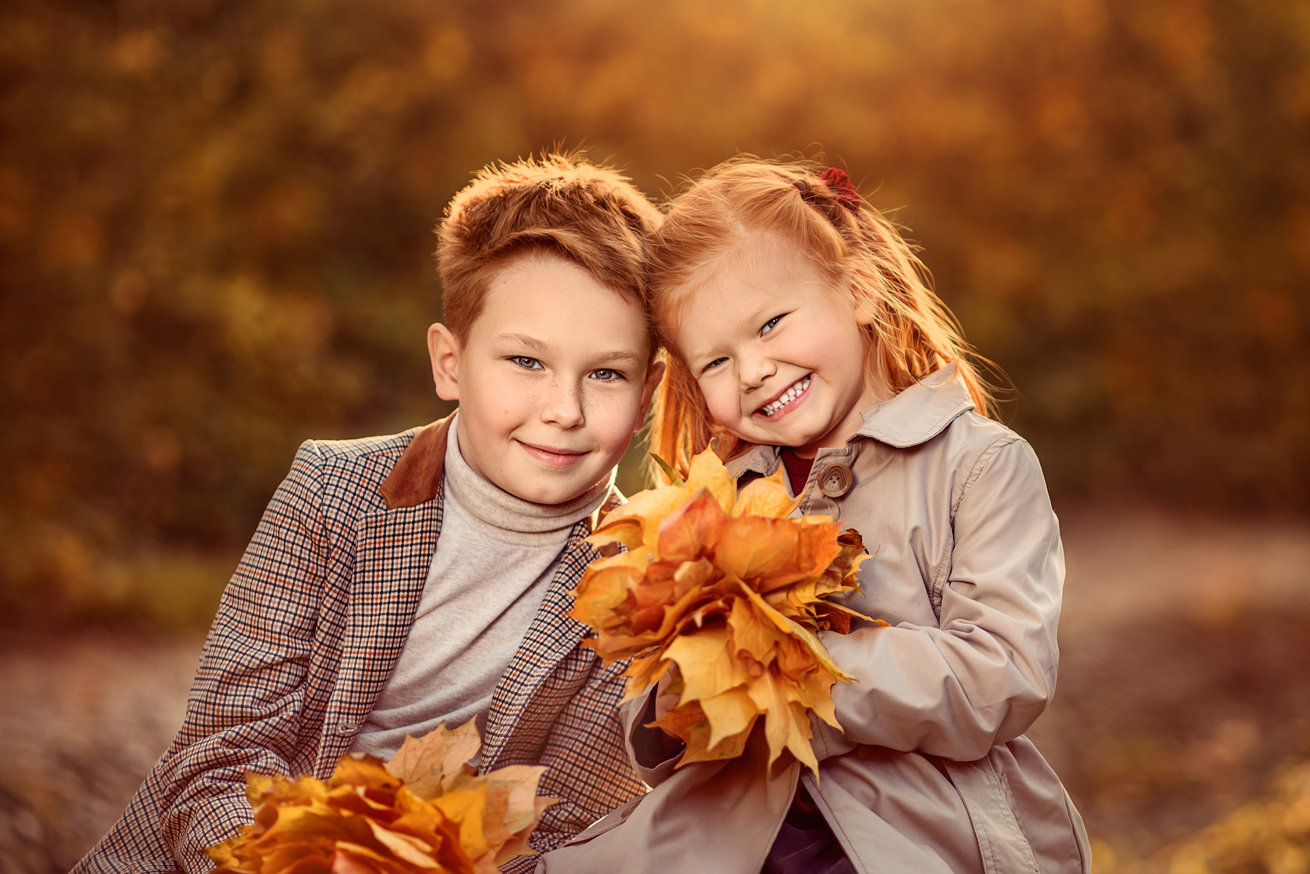 Рыжие брат и сестра с букетами из осенних листьев в парке.