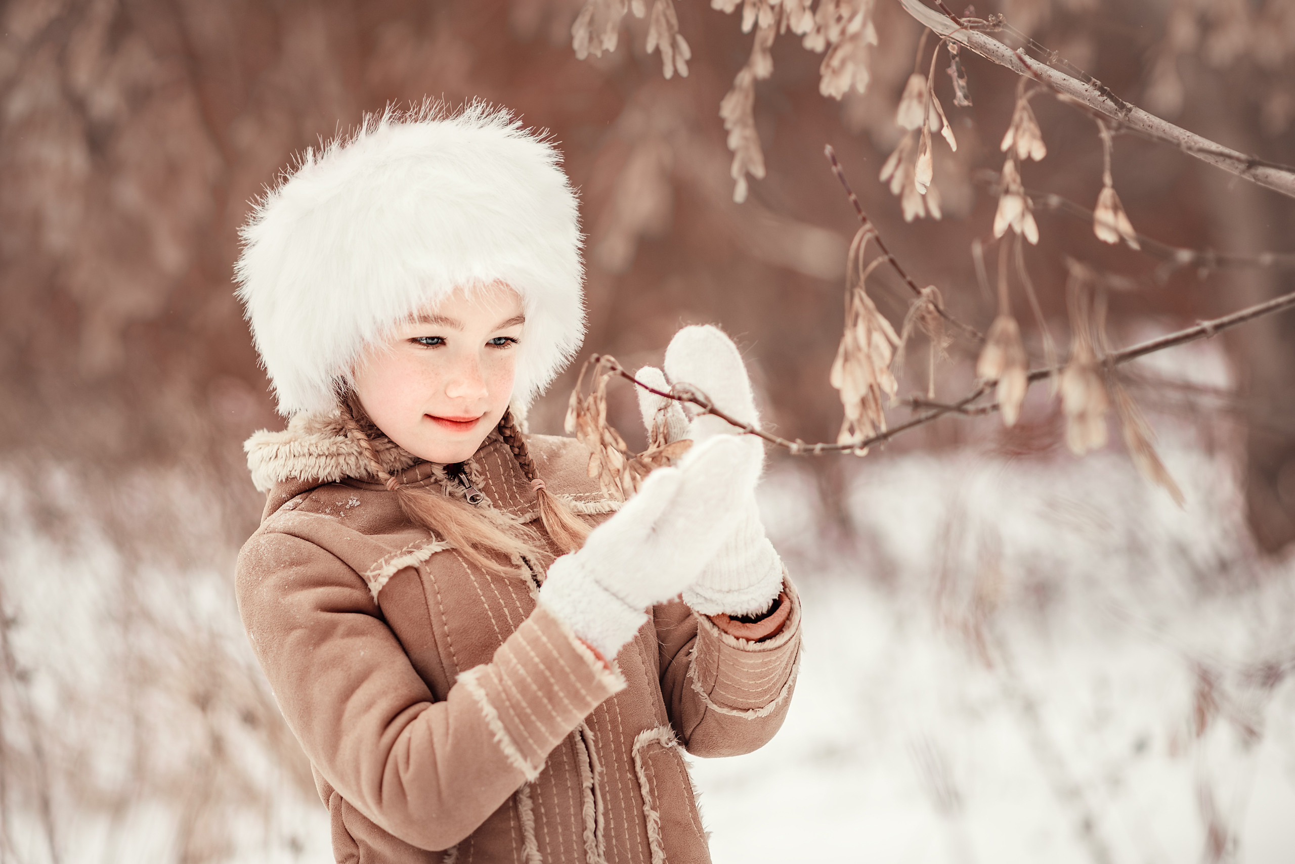 Девочка на фоне зимнего пейзажа трогает "вертолётики" на дереве.