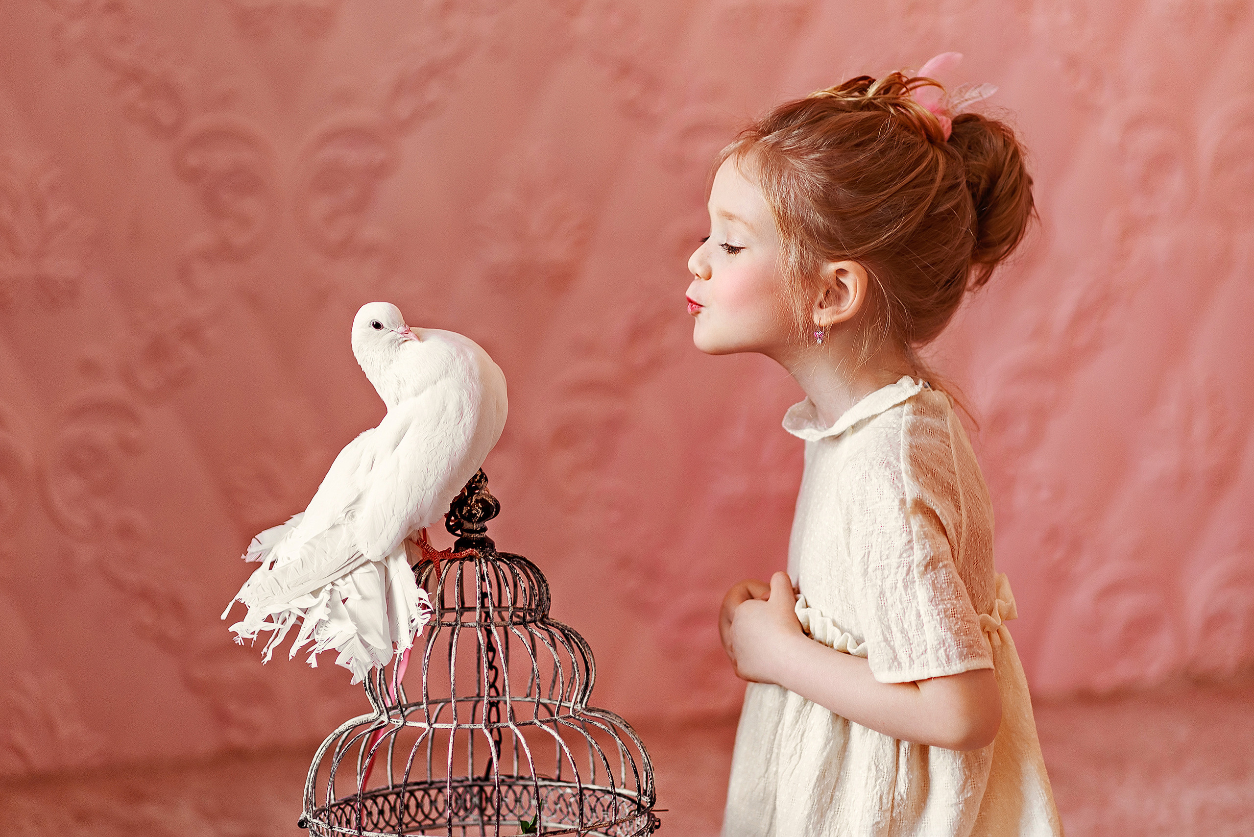Девочка в студии смотрит на белого голубя, сидящего на клетке.