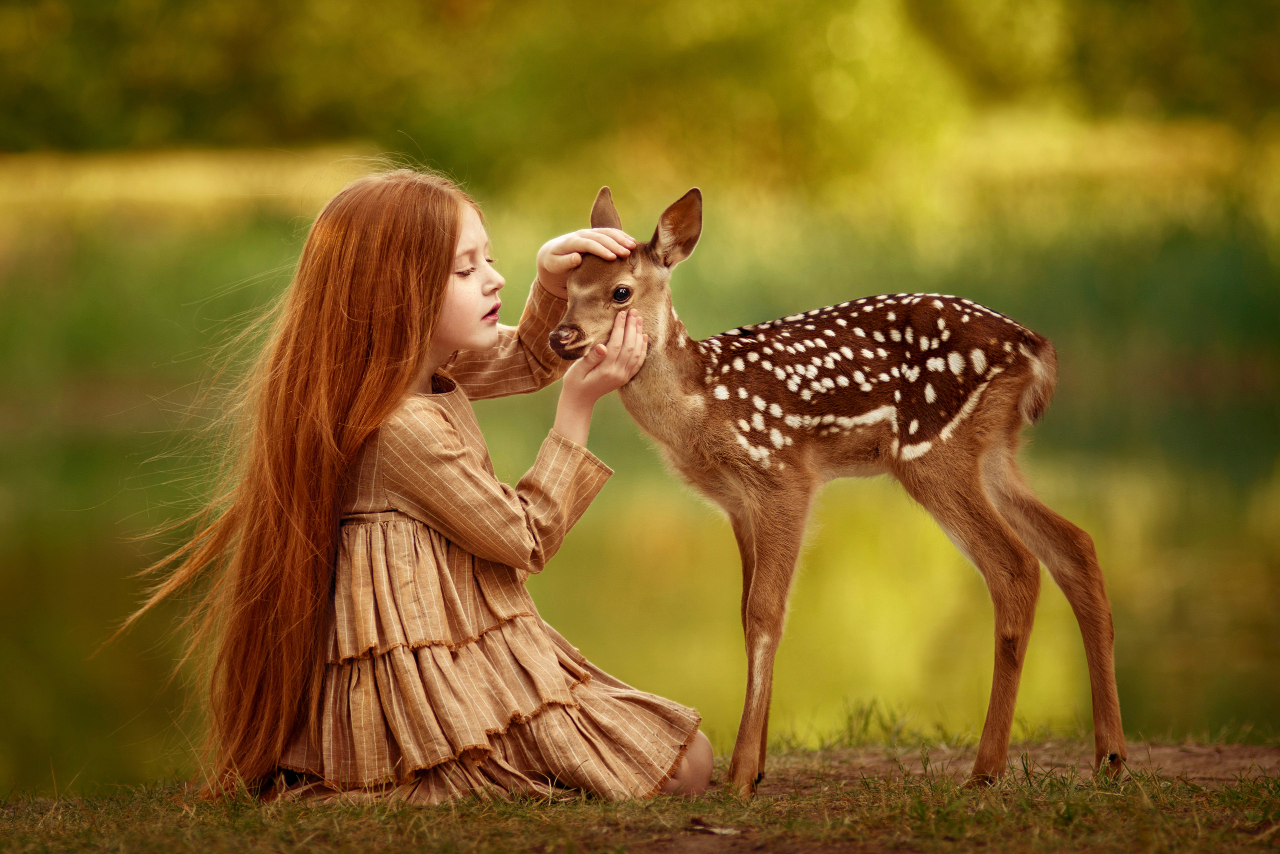 Рыжеволосая девочка гладит мордочке оленёнка бэмби.