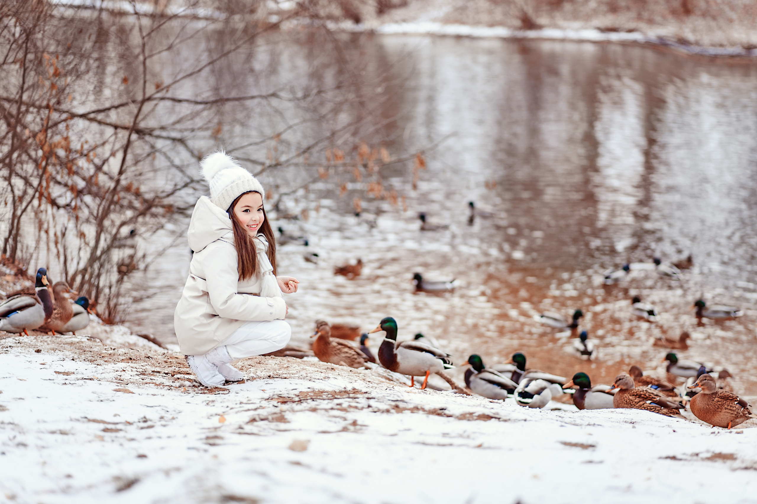 Девочка на берегу реки кормит уток зимой.