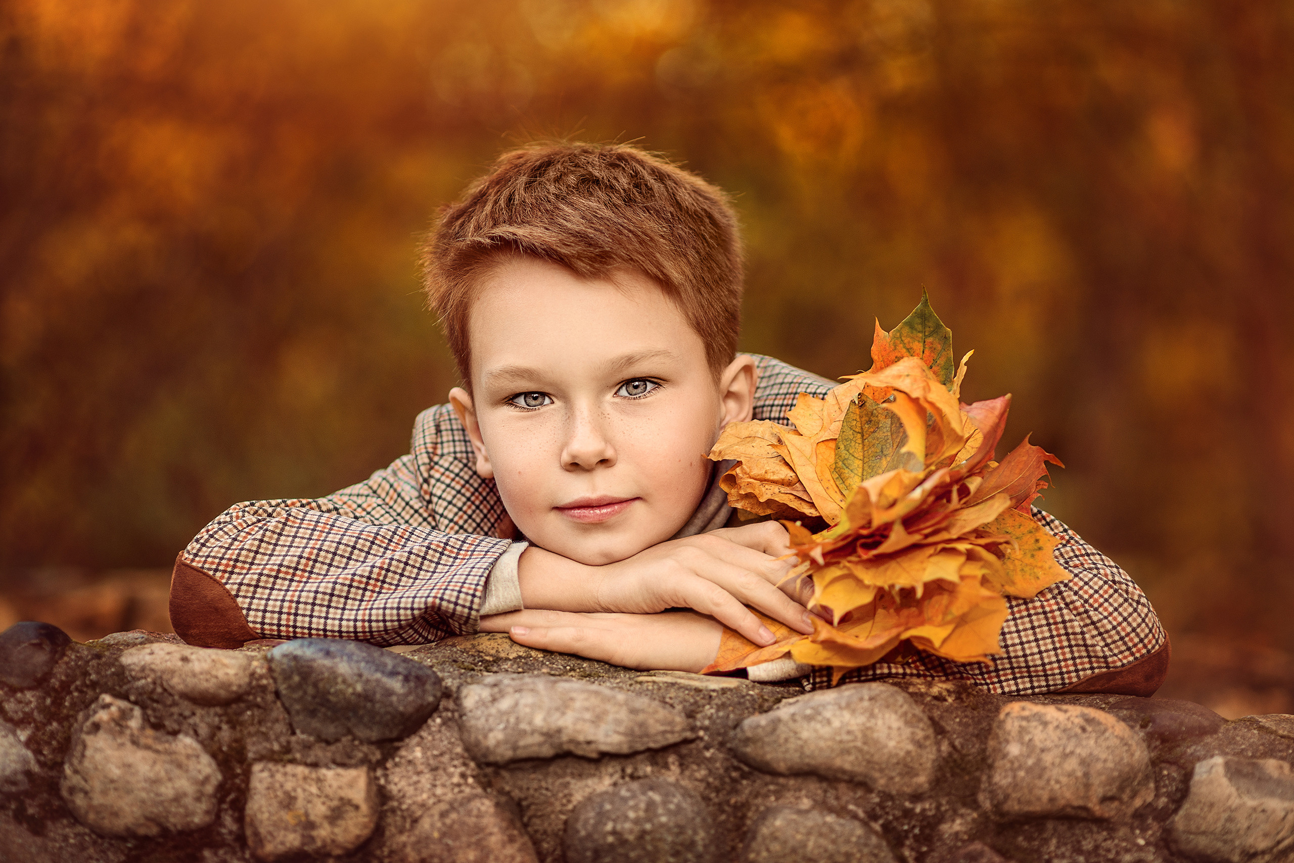 Портрет мальчика с букетом из листьев на фоне осеннего пейзажа.