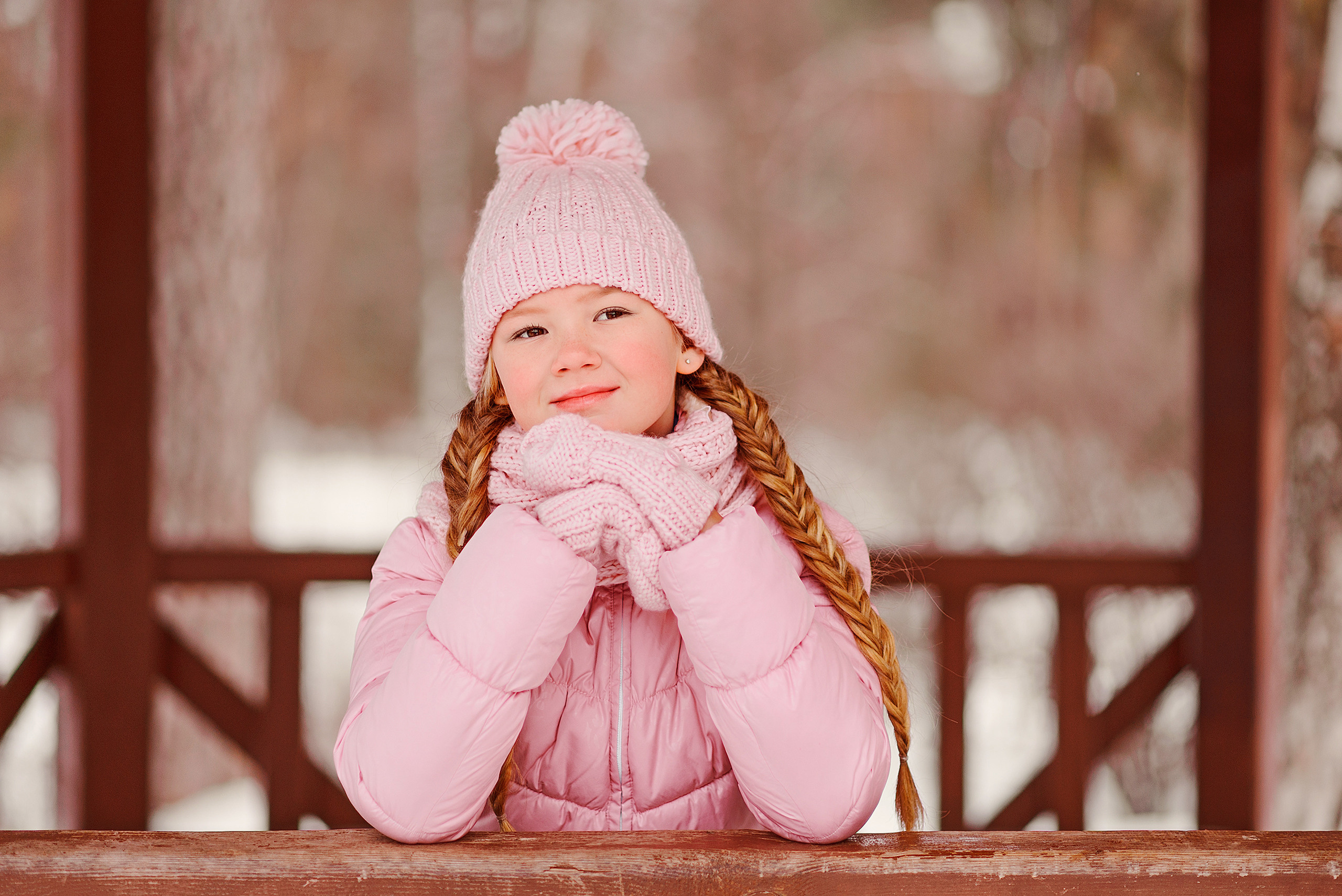 Девочка в розовой куртке сидит, задумавшись, в зимней беседке.