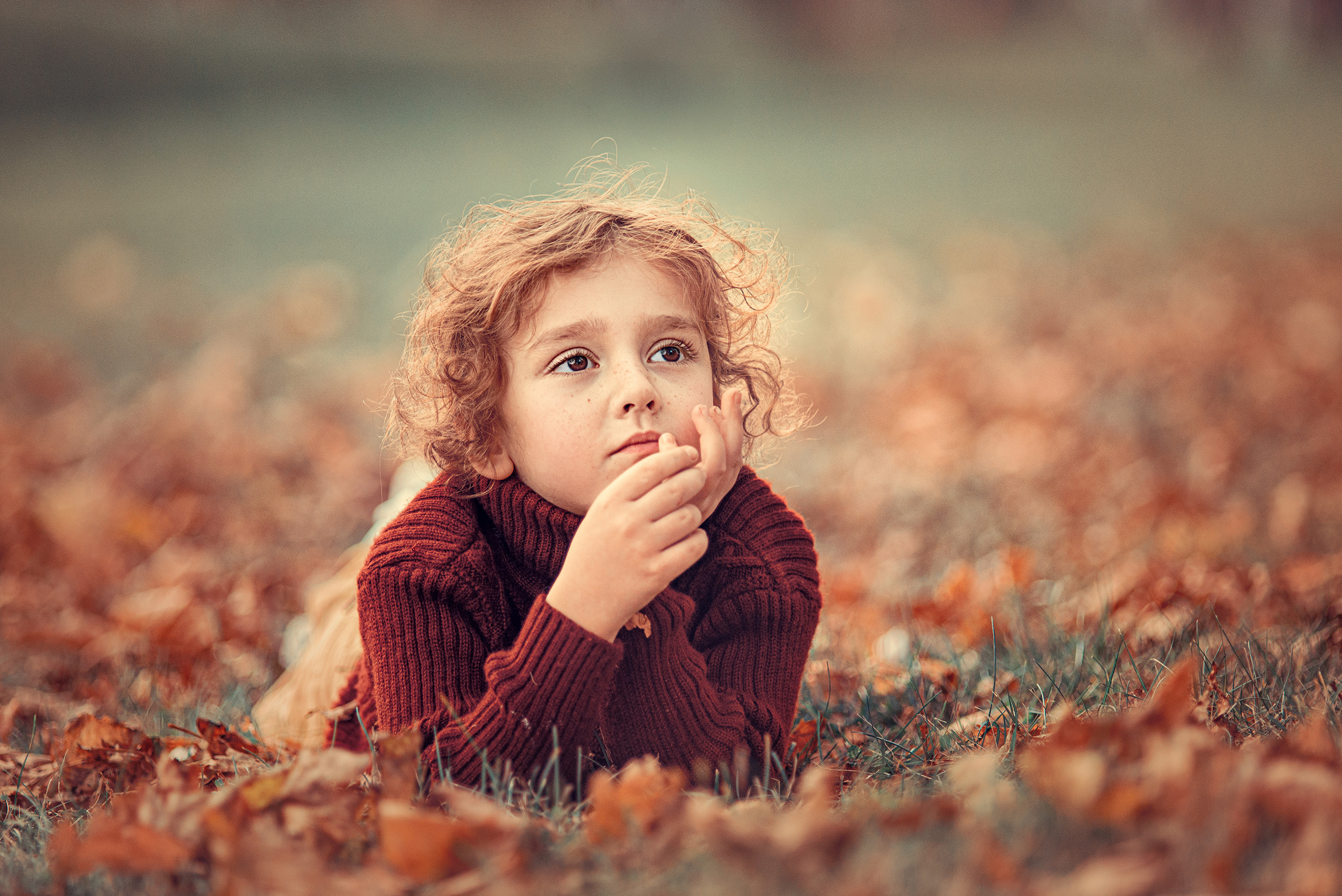 Мальчик задумчиво лежит на осенней листве во время прогулки в парке.