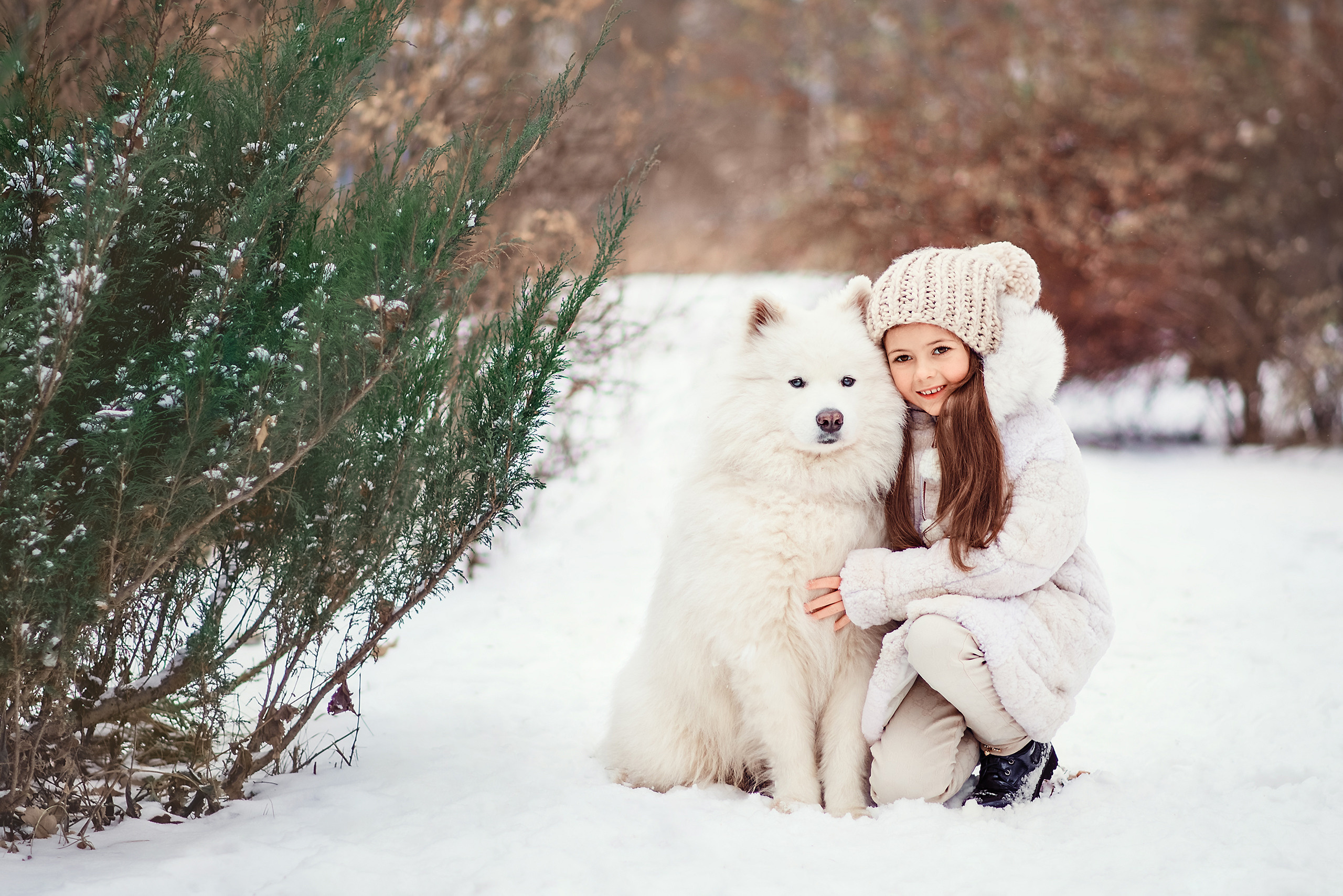 Девочка обнимает самоеда на фоне зимнего пейзажа в парке.