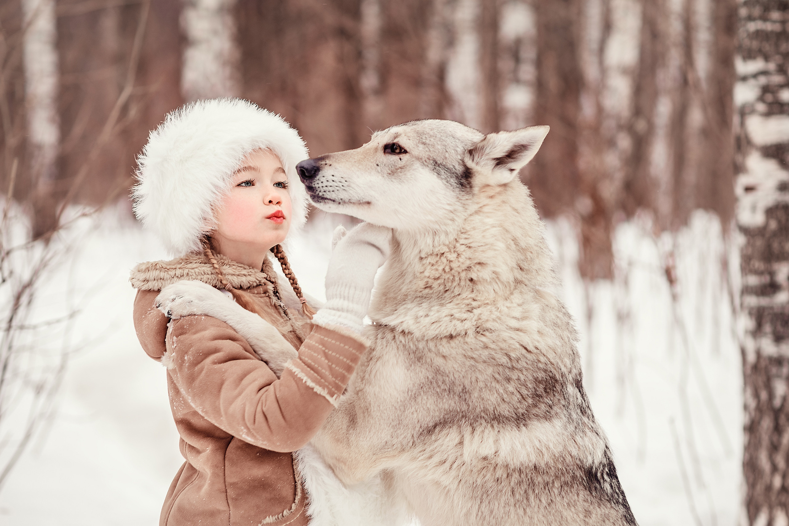 Девочка обнимает волка в зимнем лесу.