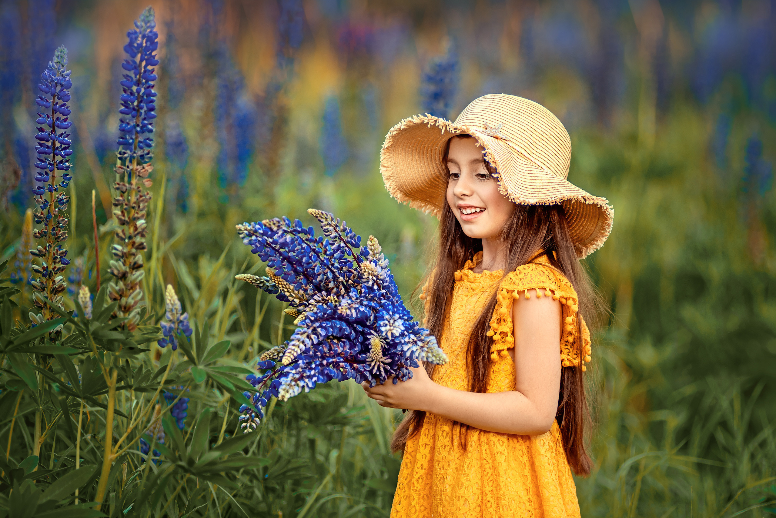 Девочка в жёлтом платье и широкополой шляпе с букетом синих люпинов.