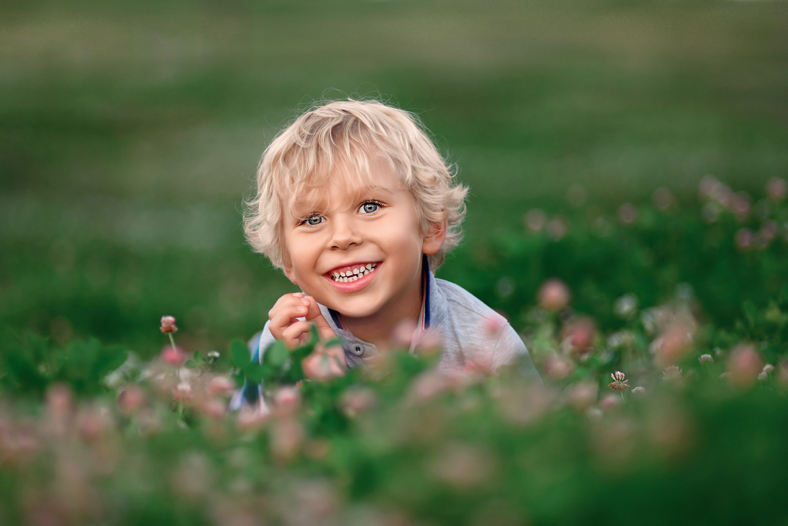 Улыбающийся мальчик лежит на траве в розовом клевере.