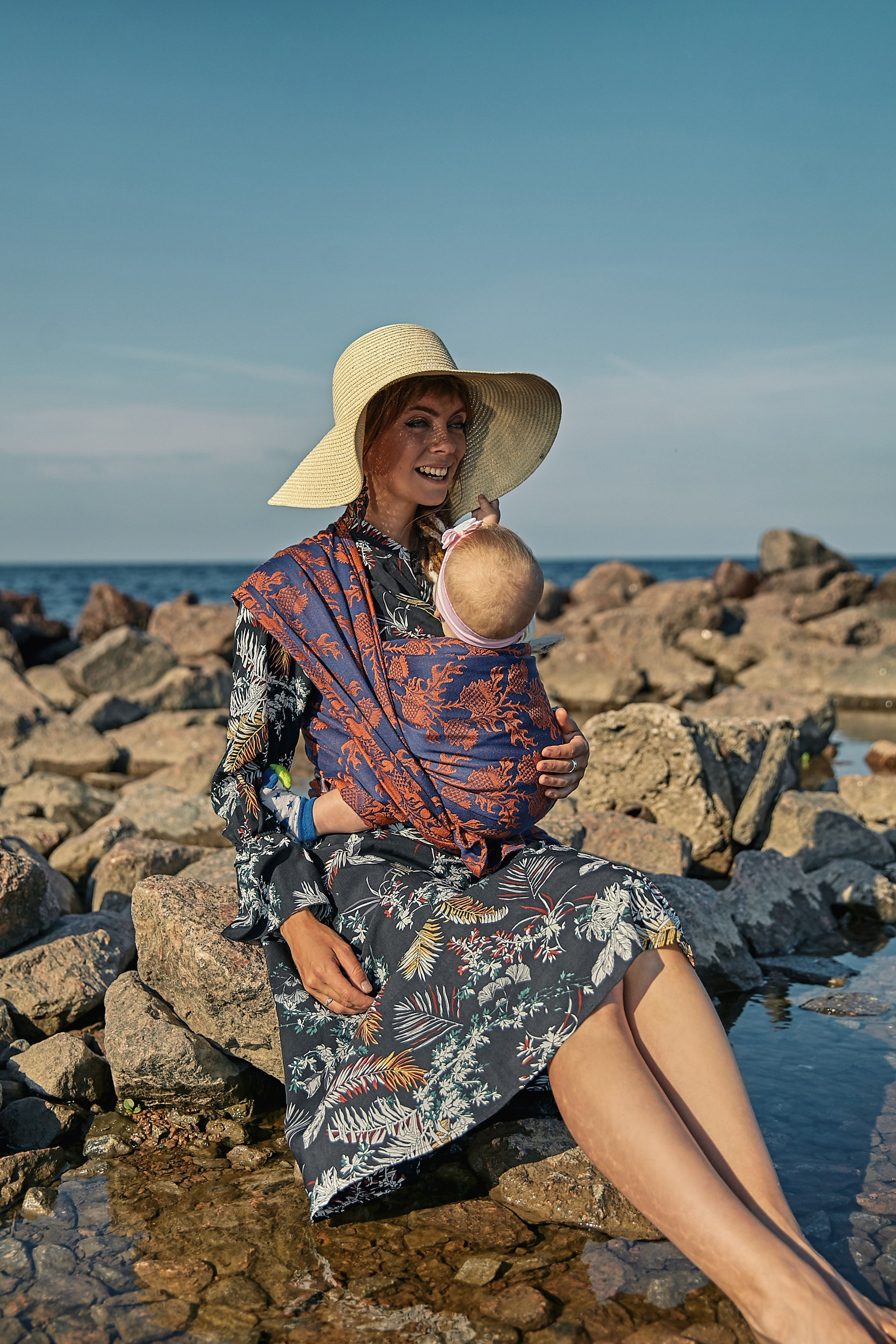 Девушка на берегу залива в черном платье и соломенной шляпе с малышом в слинге