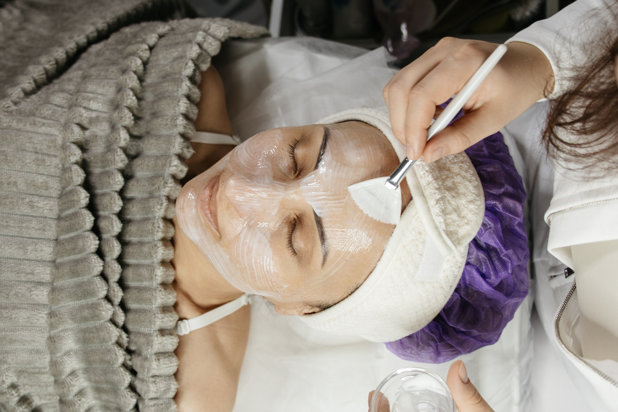 Косметолог наносит крем кисточкой, крупный план