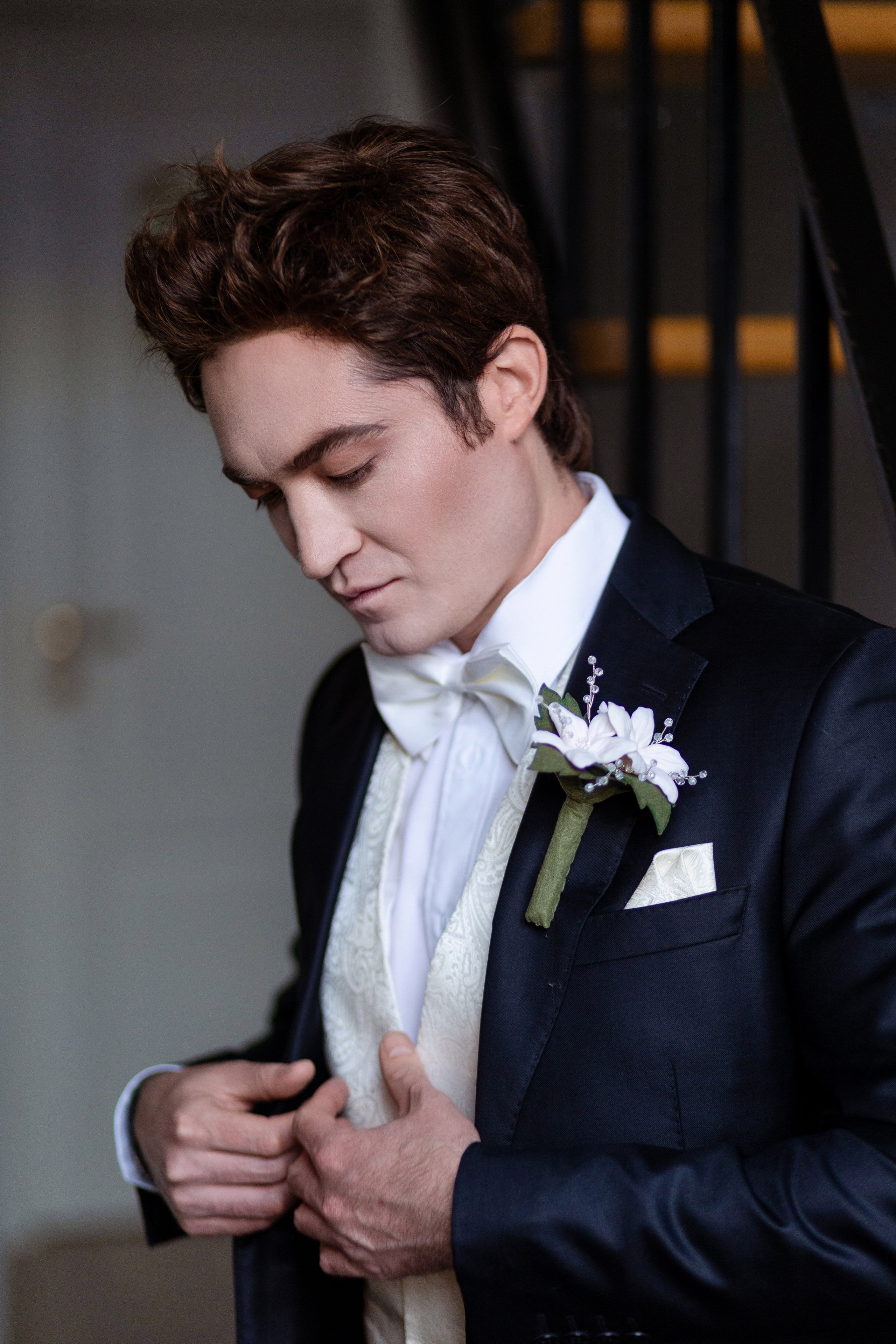 Жених на фоне лестницы поправляет красивую рубашку.