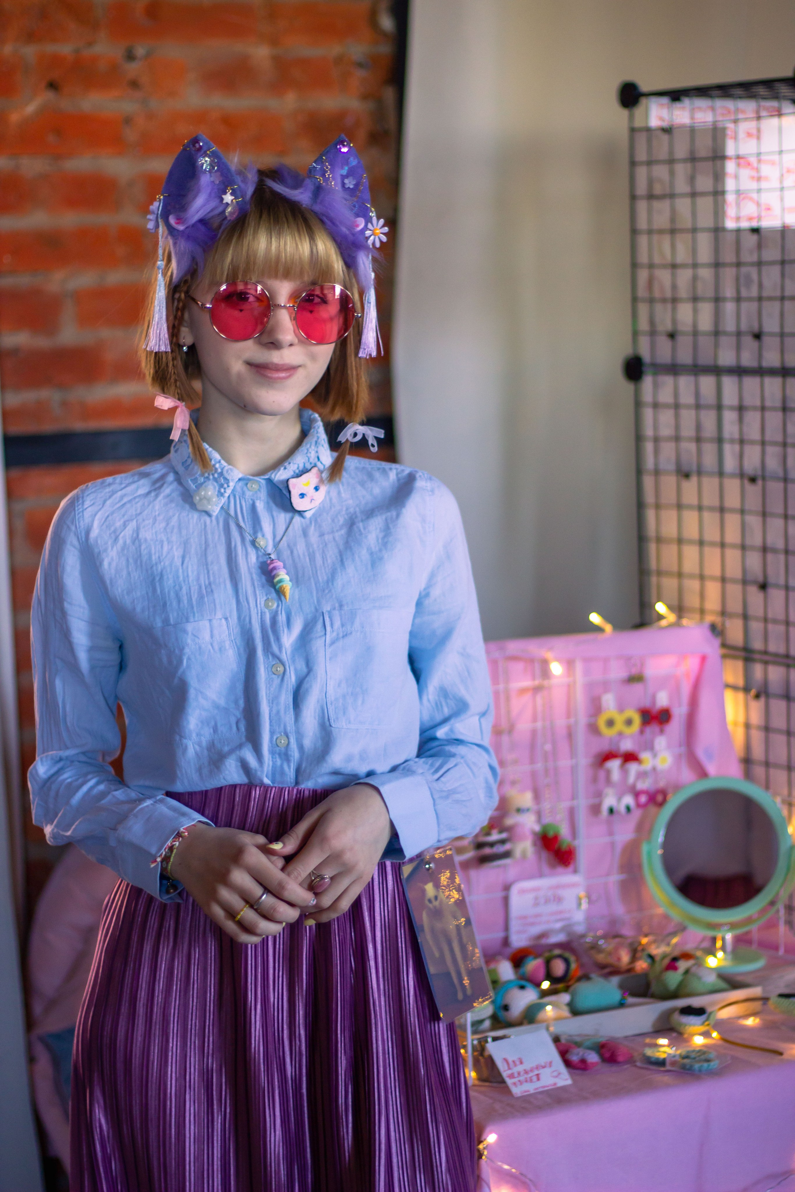 Девушка в кошачьих ушках стоит у своего столика с побрякушками