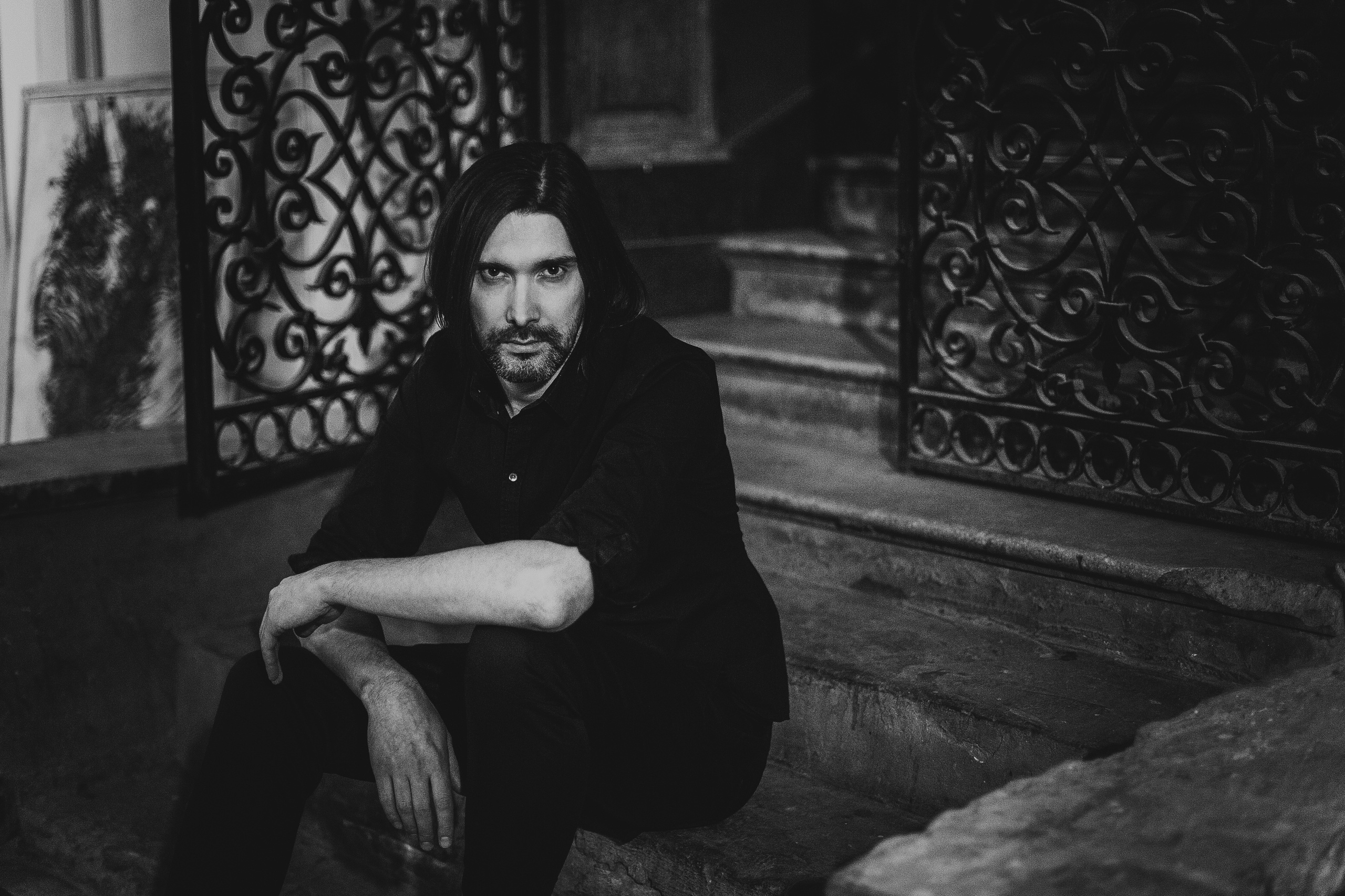 стильный парень сидит у красивой фигурной решетки ворот