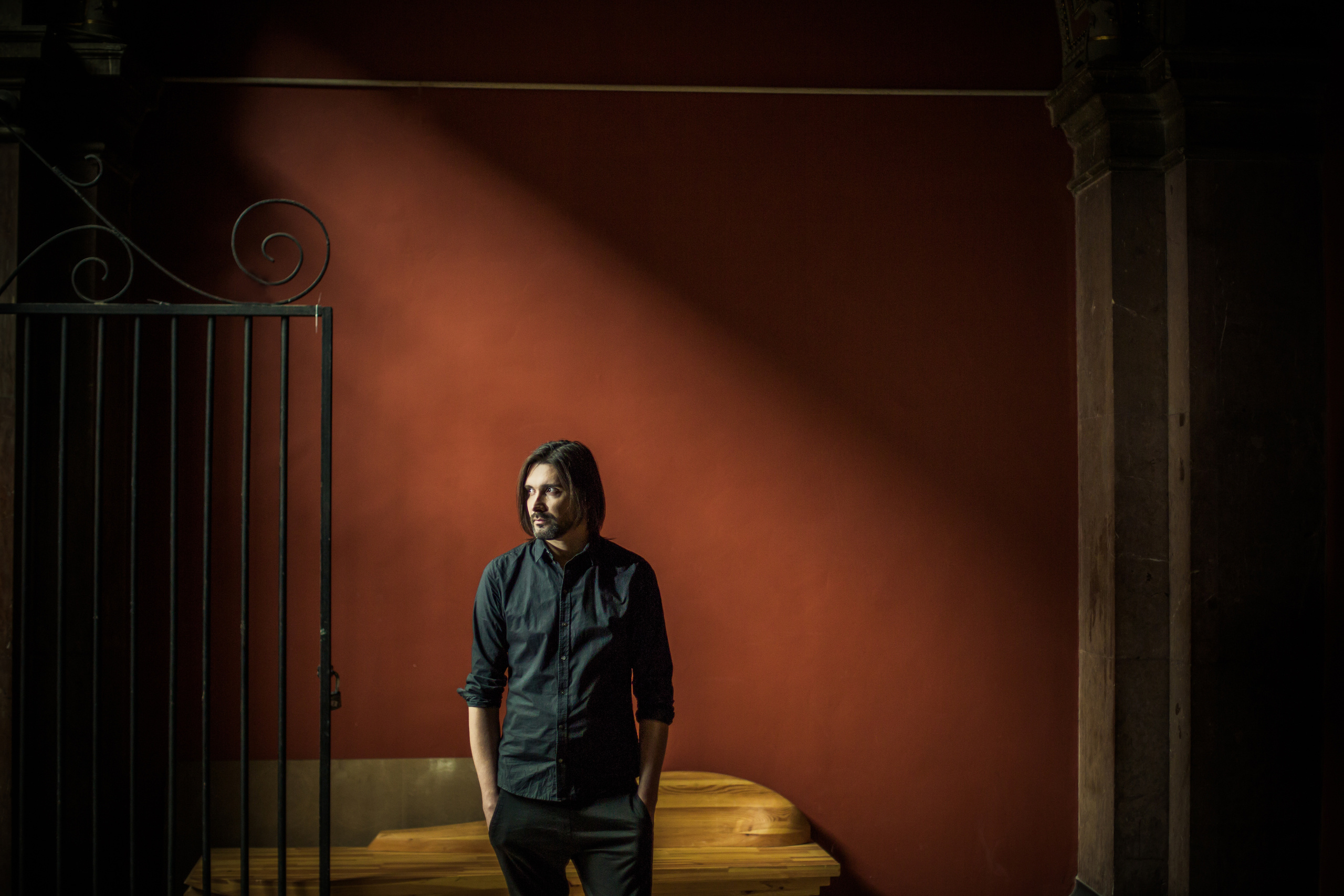 мужчина стоит с рукам в карманах у красной стены в лучах света