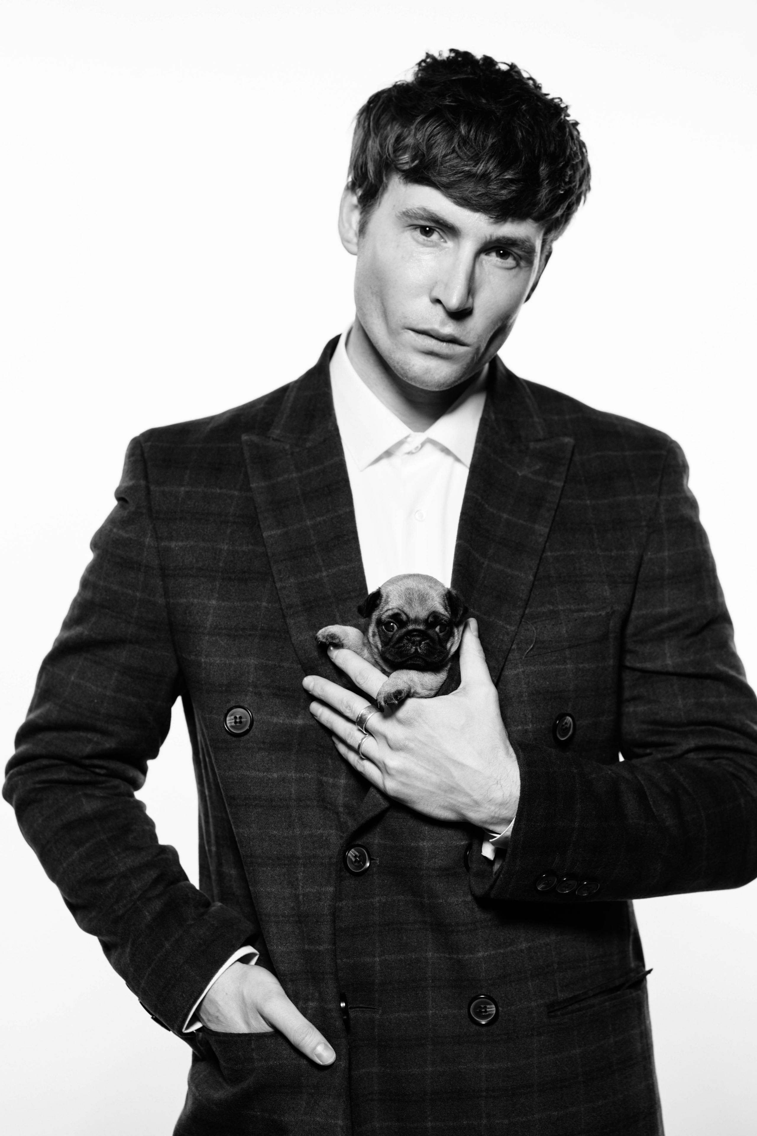 Черно-белый портрет брутального мужчины с щенком на белом студийном фоне.