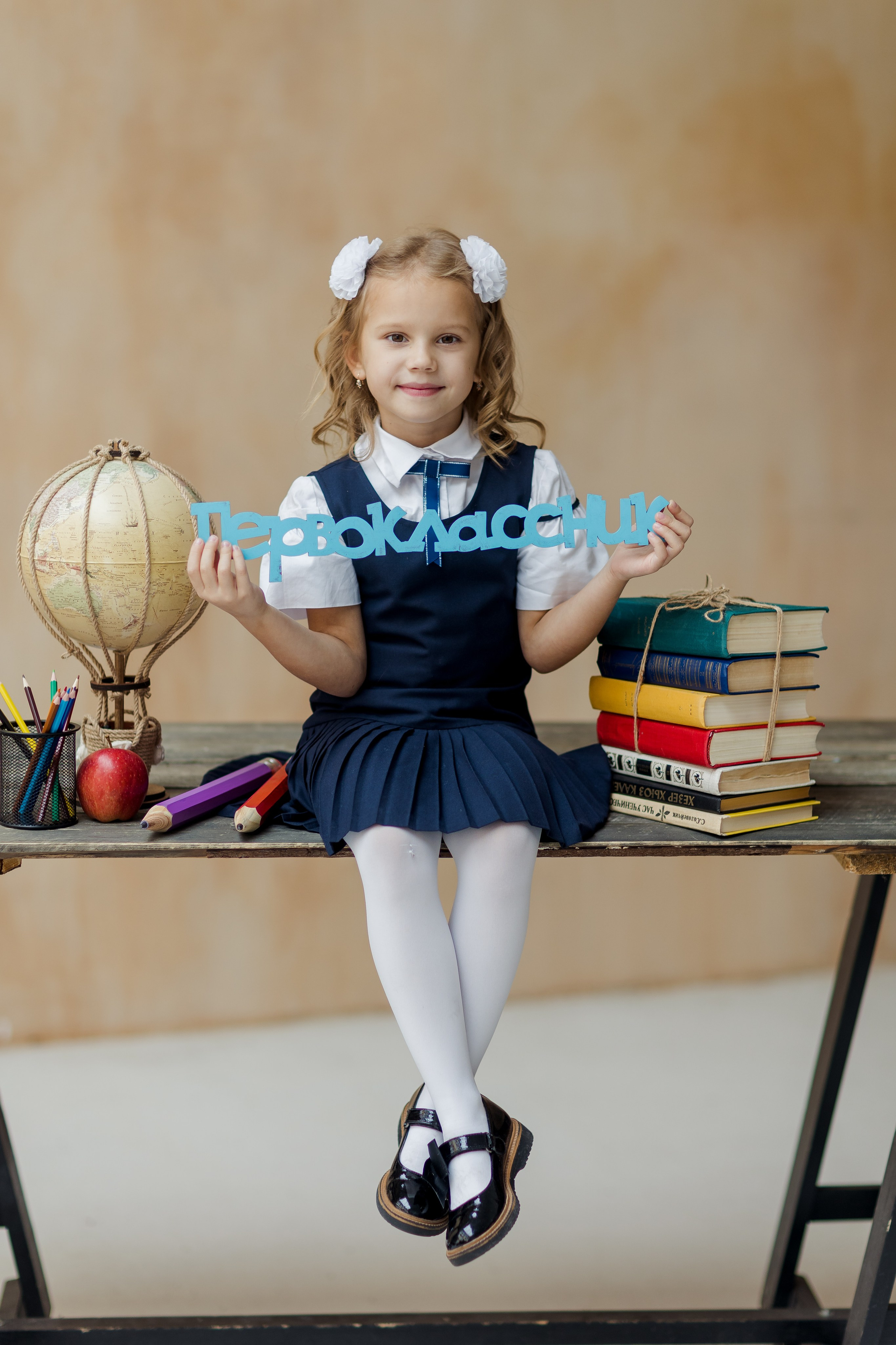 Девочка сидит на столе с книгами и глобусом с надписью первоклассник