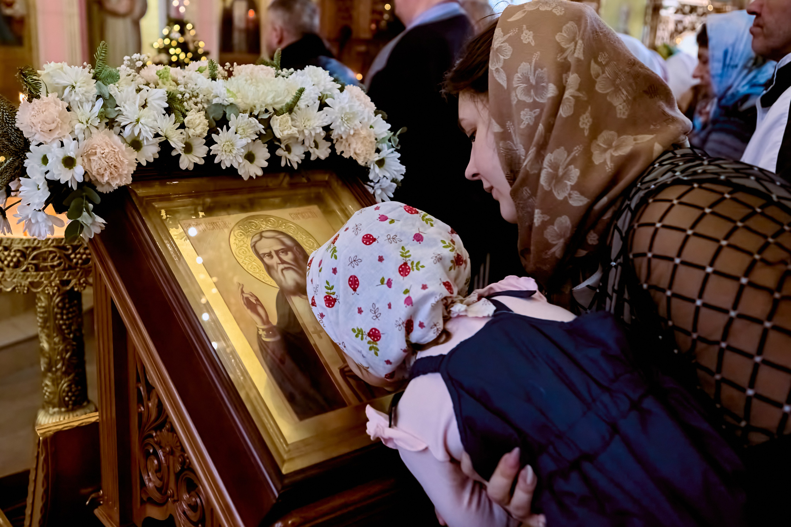 Маленькая девочка на руках у мамы приклоняет голову перед иконой на аналое