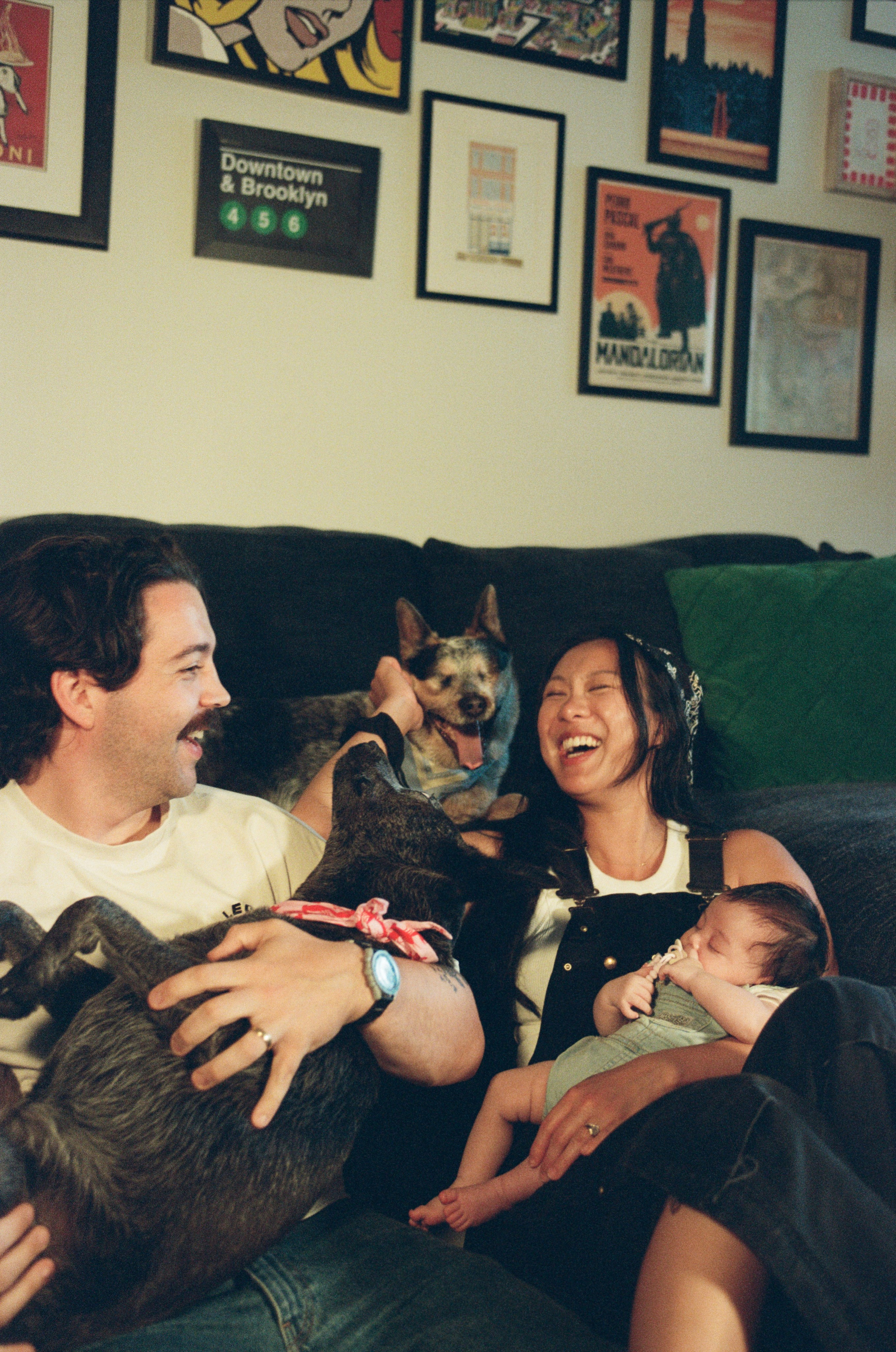 a family of 5 including 2 dogs captured on film in their living room the dogs up on the couch and parents holding a baby girl are on the floor