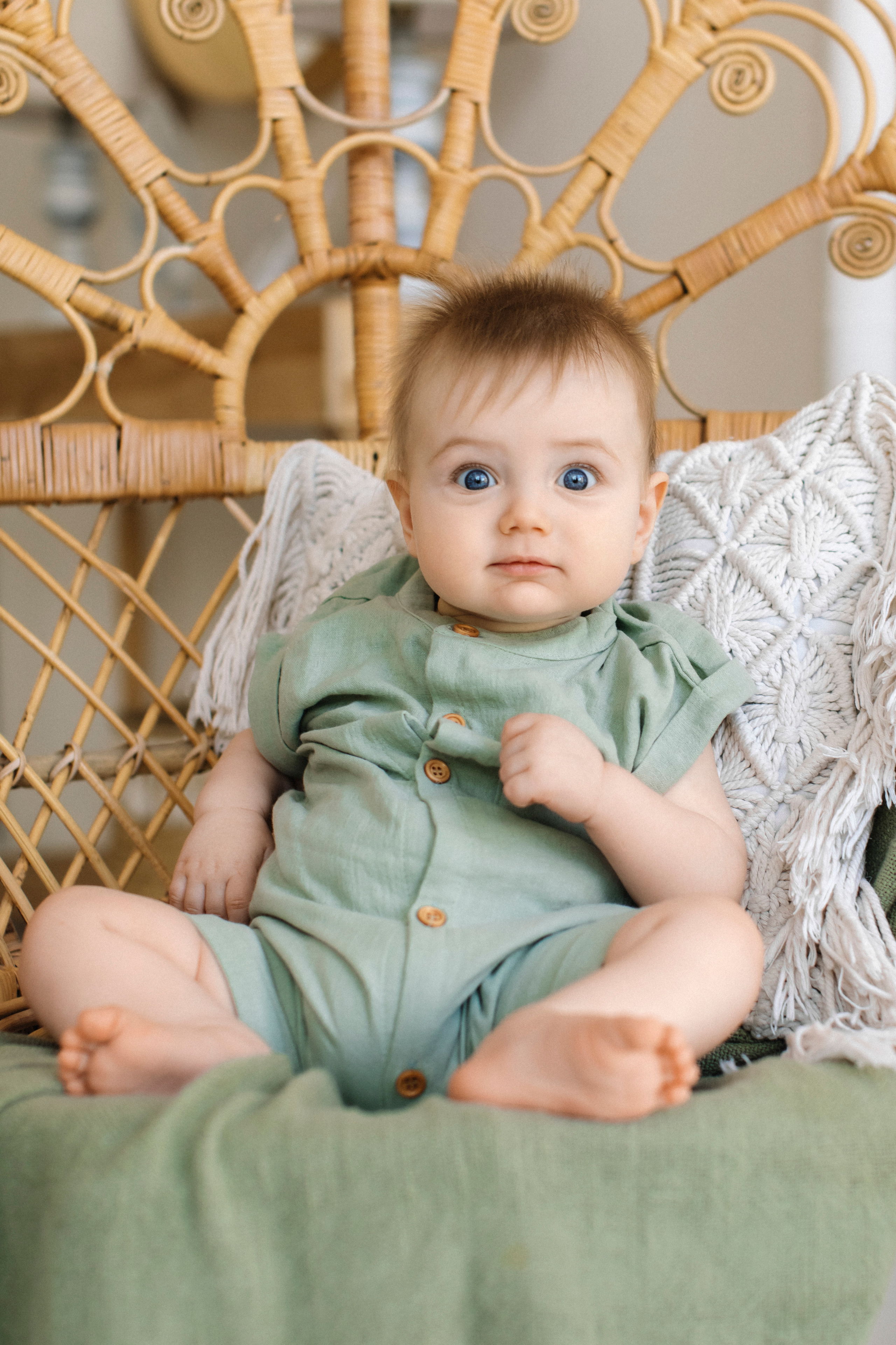 Мальчик 7 месяцев в зеленом. комбинезоне сидит в кресле