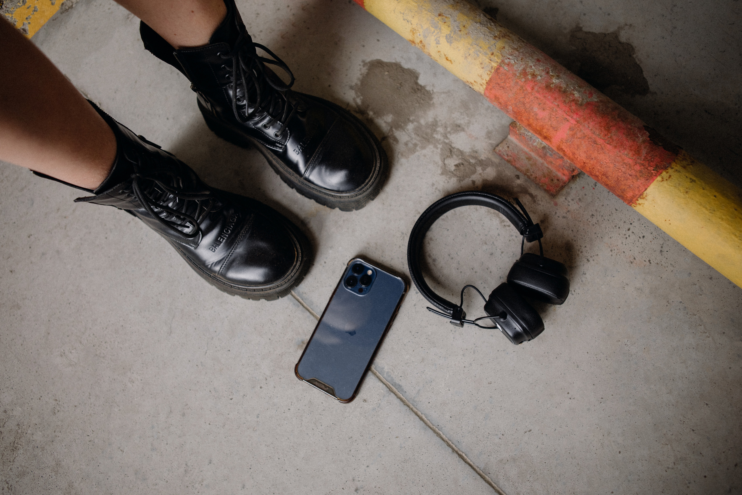 Ноги в черных ботинках рядом с телефоном iPhone и наушниками Marshall 