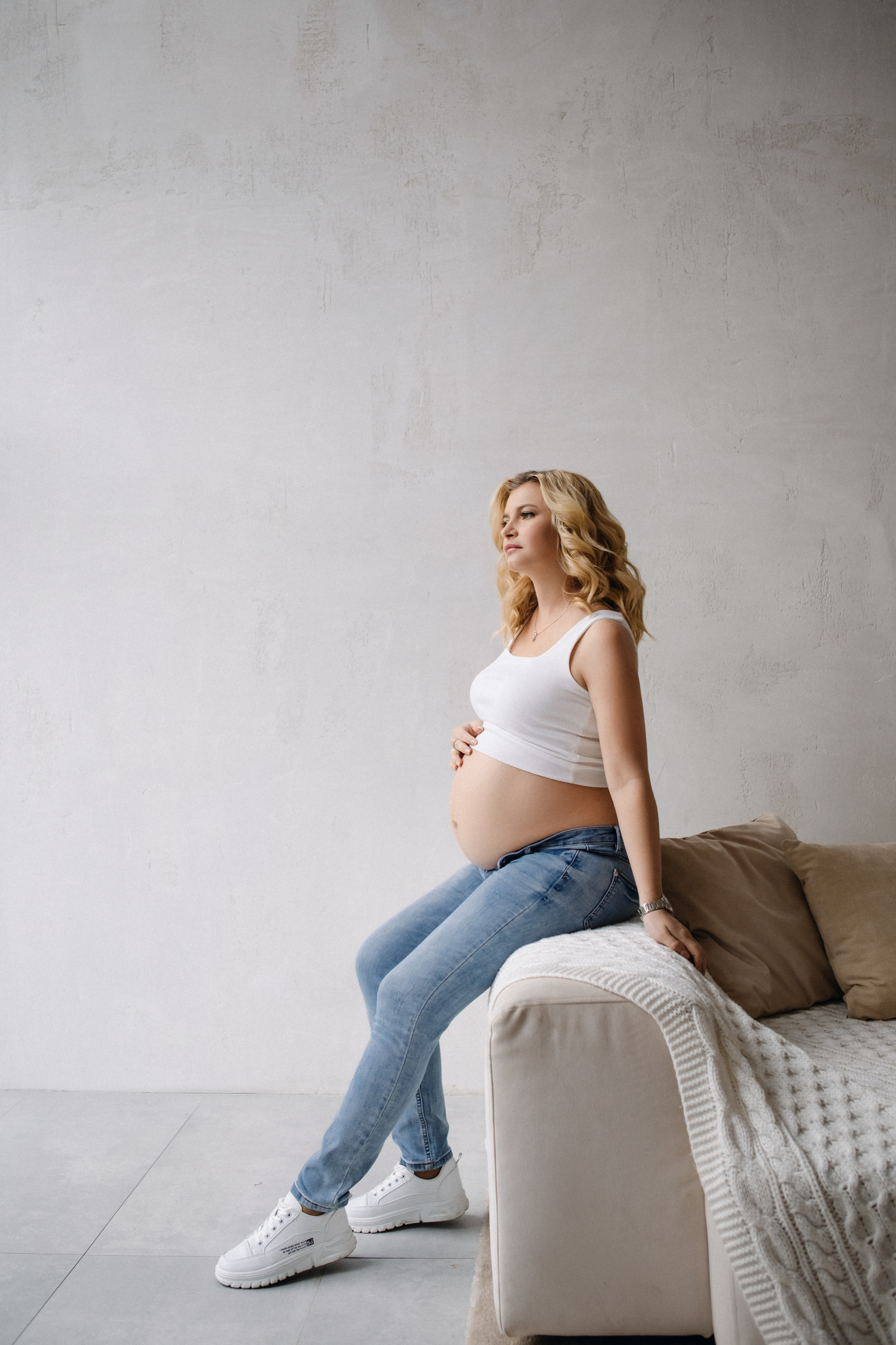 Беременная в джинсах белом топе и белых кроссовках в студии Мимика