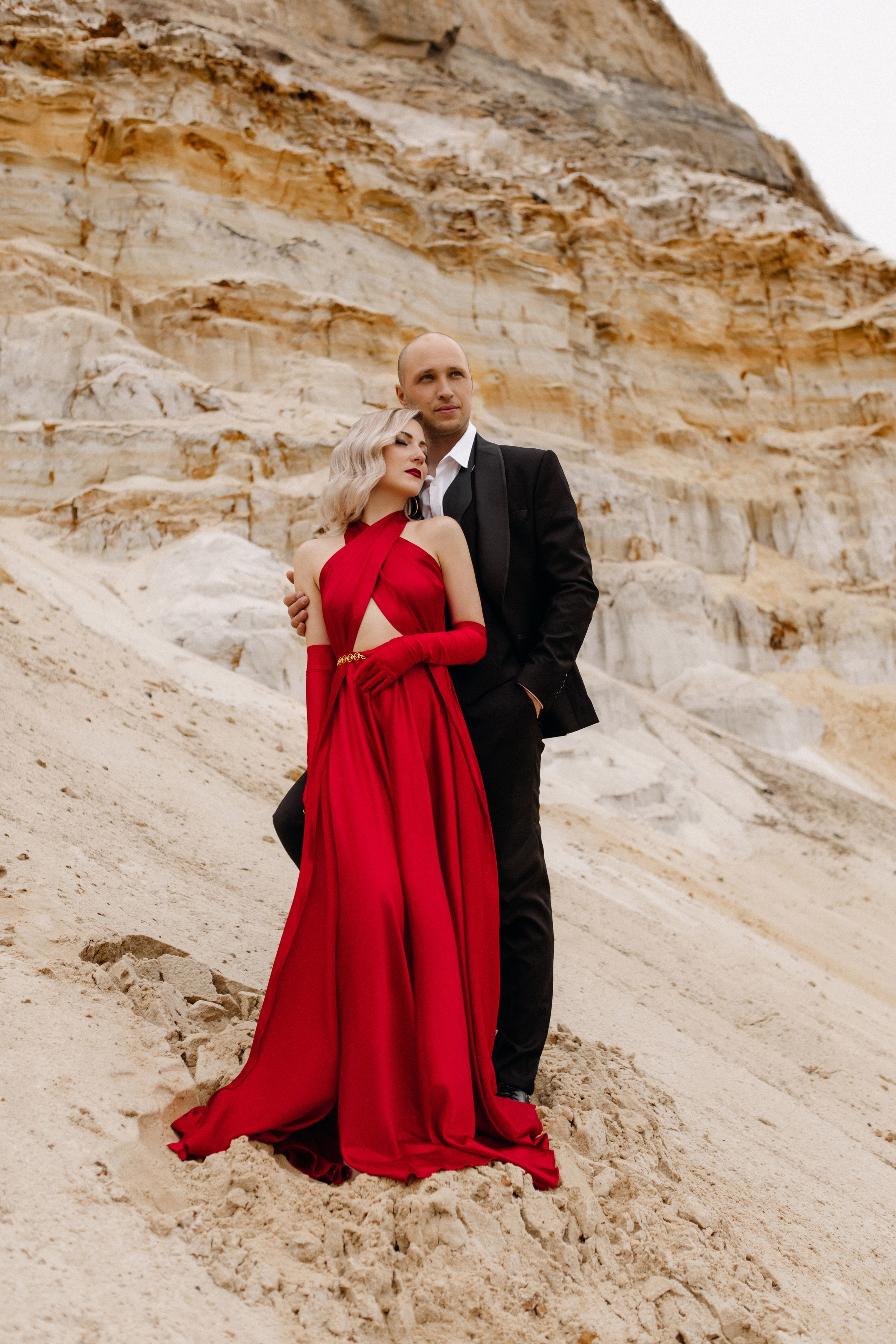 Девушка в красном платье и красными перчатками посреди песка