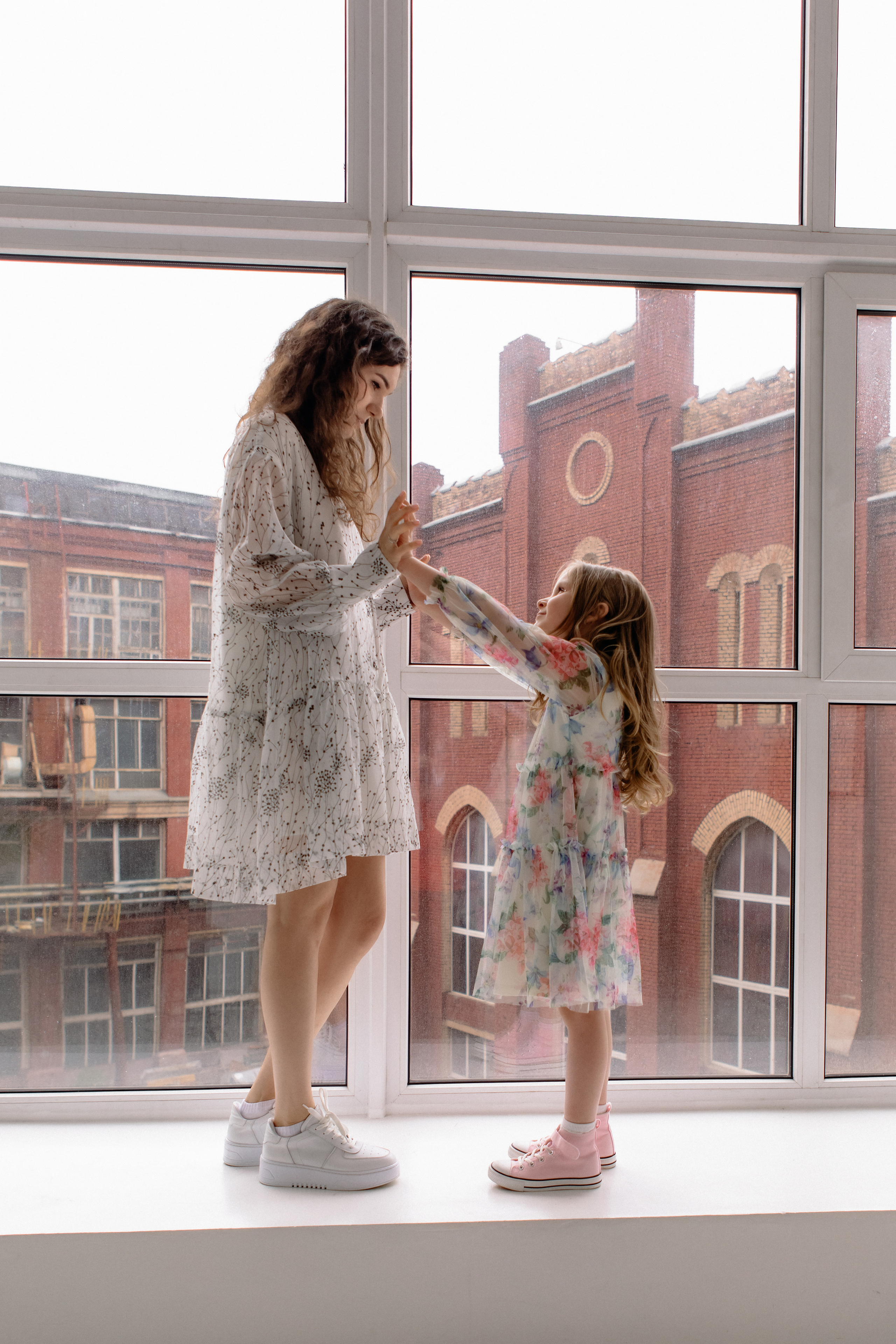 Мама и дочка в платьях стоят на окне