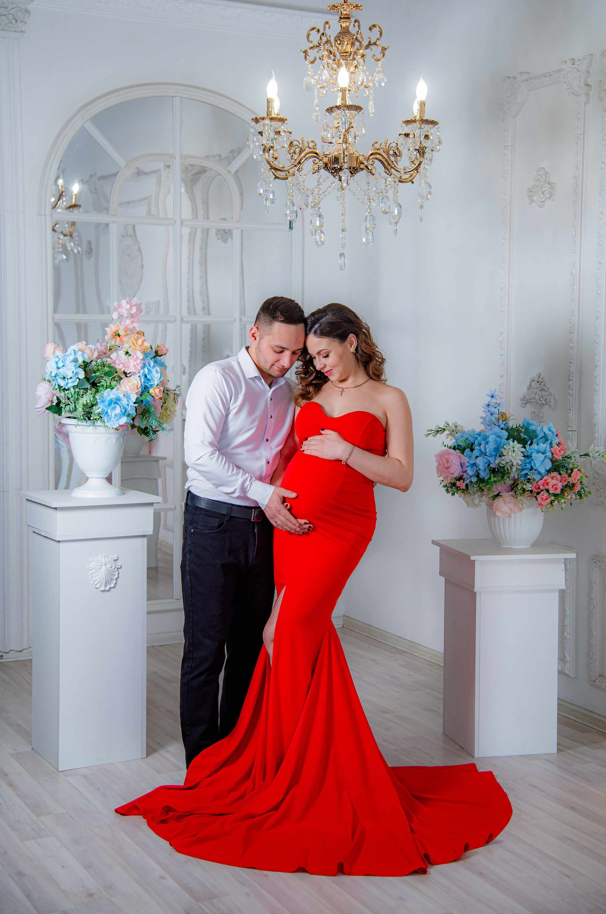 Фотосессия беременных в фотостудии в Уфе: будущая мама в элегантном платье из проката, с профессиональным макияжем и прической. Она счастливо позирует на фоне стильного интерьера, а рядом ее муж и члены семьи. Фотограф помогает в позировании, создавая теплую и уютную атмосферу, отражающую красоту и нежность материнства